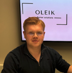 A young man with glasses and blonde hair sits in front of a screen displaying the OLEIK logo and the slogan 'Better solutions.'