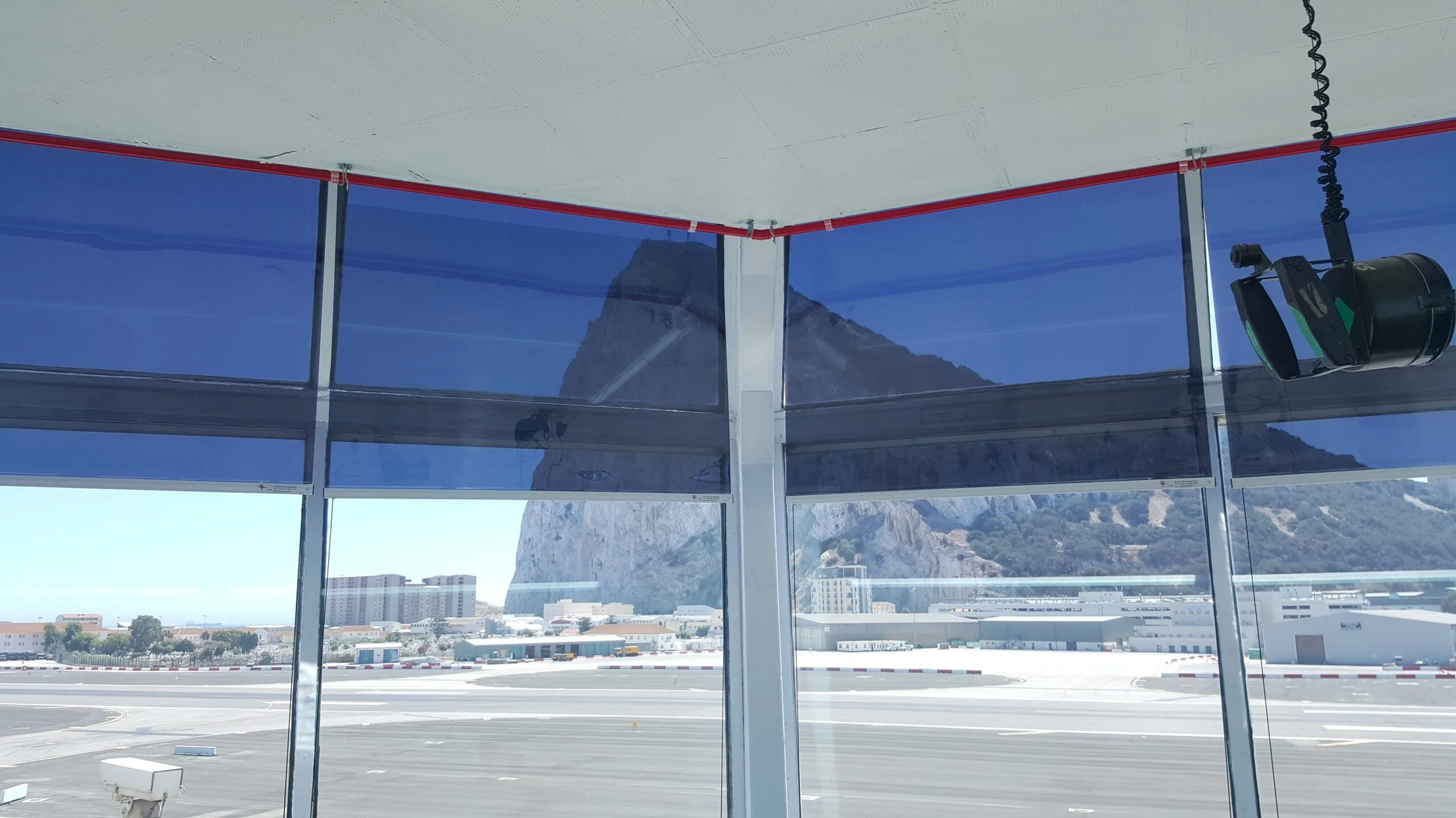 View from inside a glass-walled airport terminal with mountains in the background and city buildings below, seen through large windows.