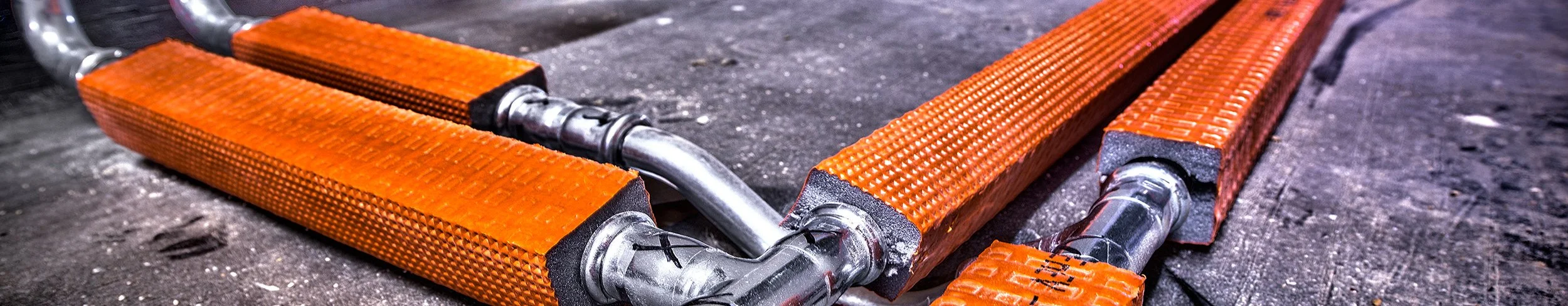 Orange robotic heating mats connected with metal piping on a dark floor.