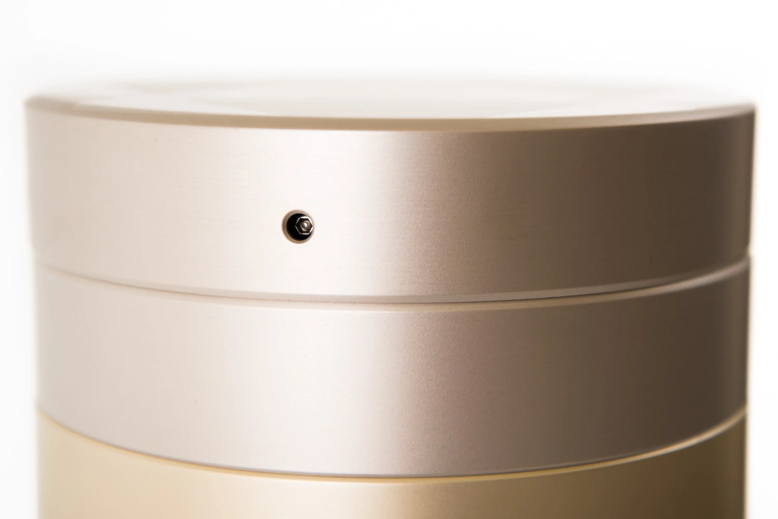 Close-up of a metallic beige-colored cylindrical device with a small black screw or sensor on the front.