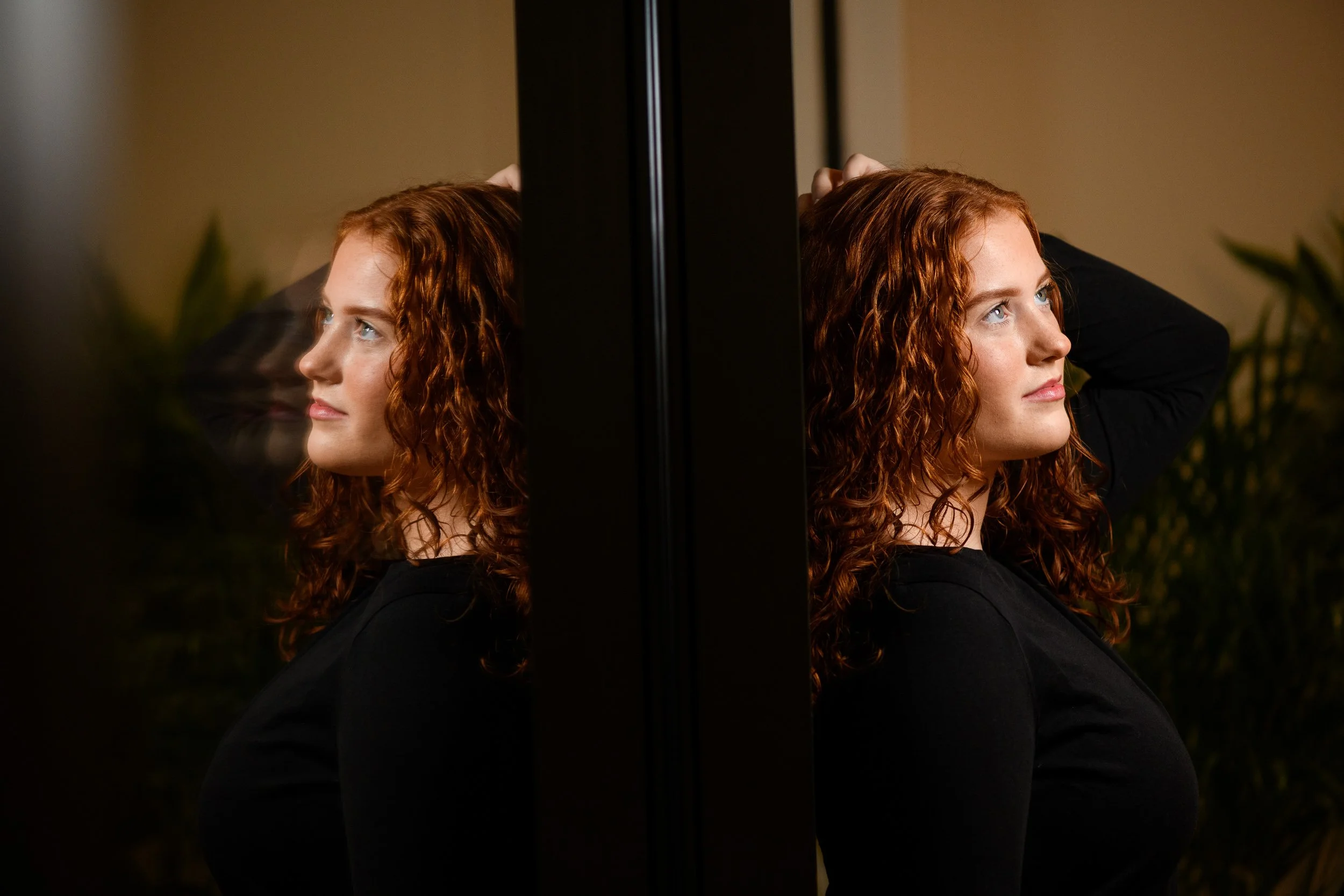 Artistic mirror portrait of a woman with curly red hair and soft expression
