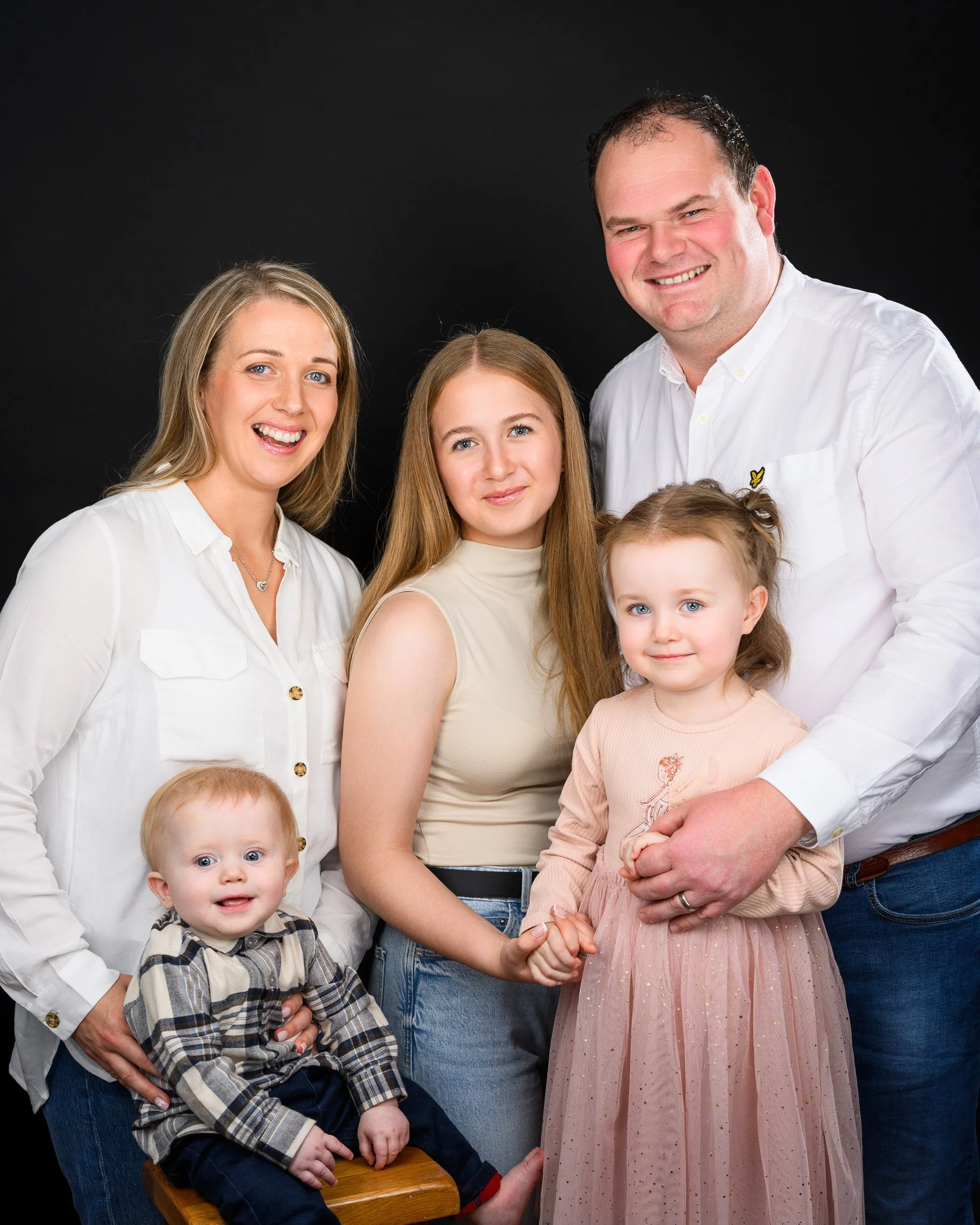 Family portrait of five people including two children, posed together against a black background.
