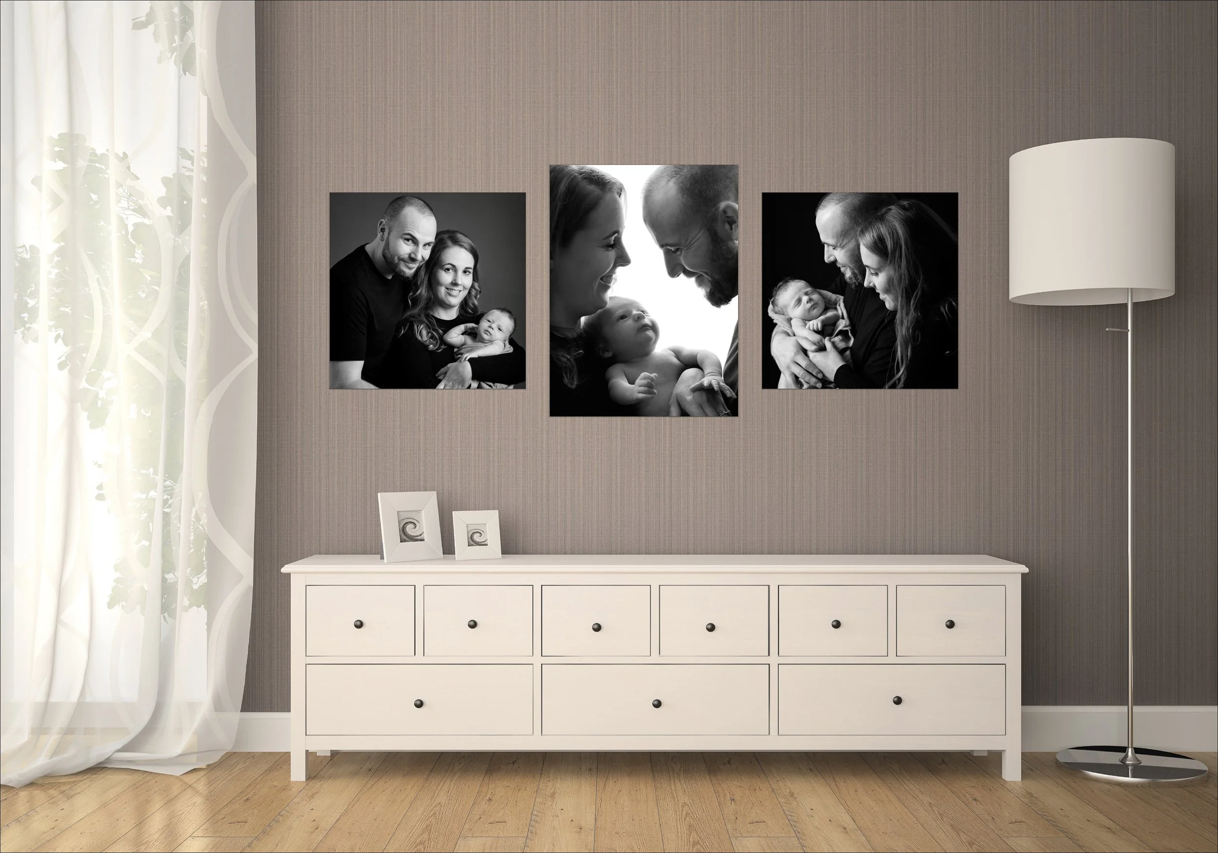 Black and white family portraits displayed above a dresser in a softly lit living space.
