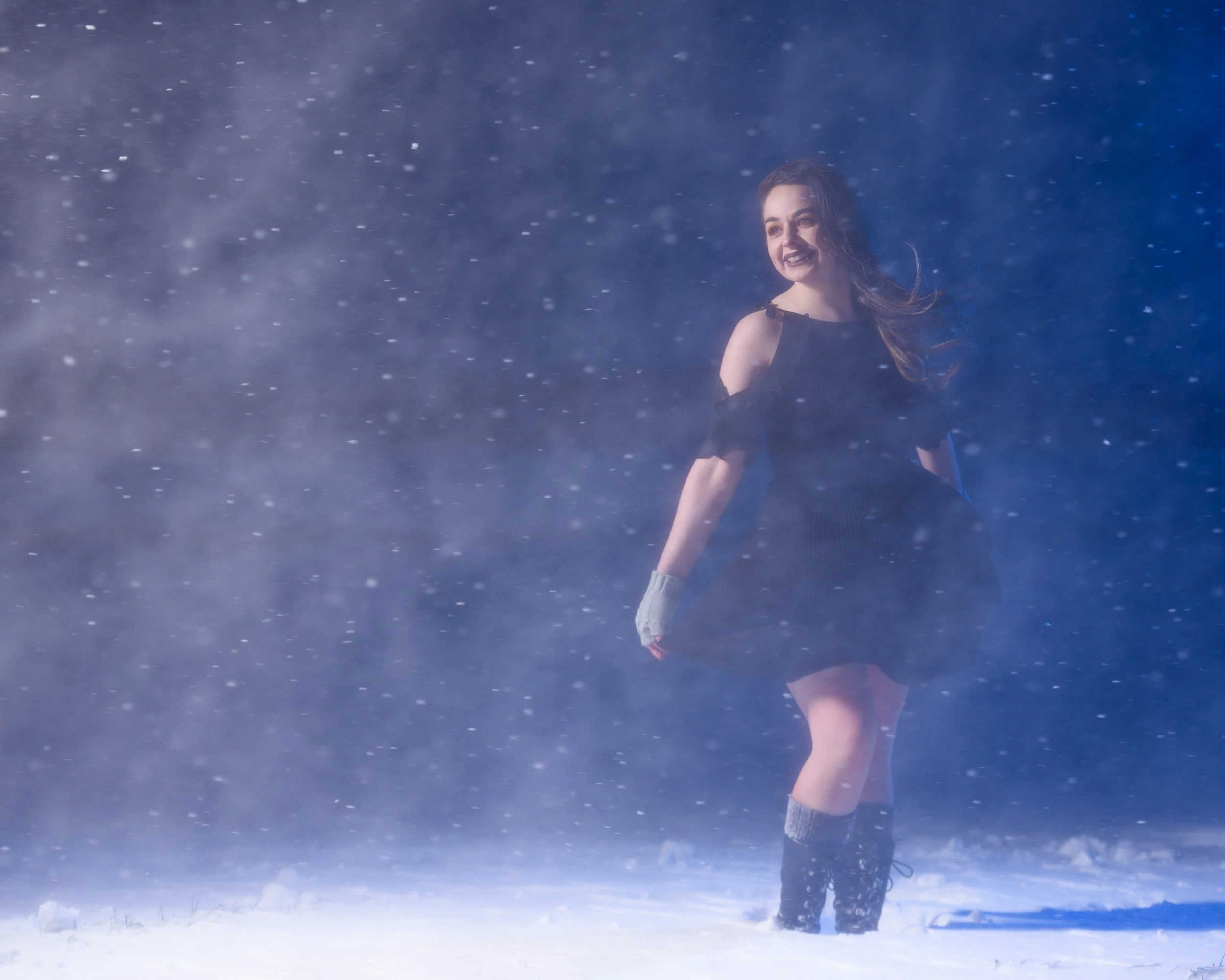 Outdoor winter portrait of a woman smiling in snowfall wearing boots and gloves
