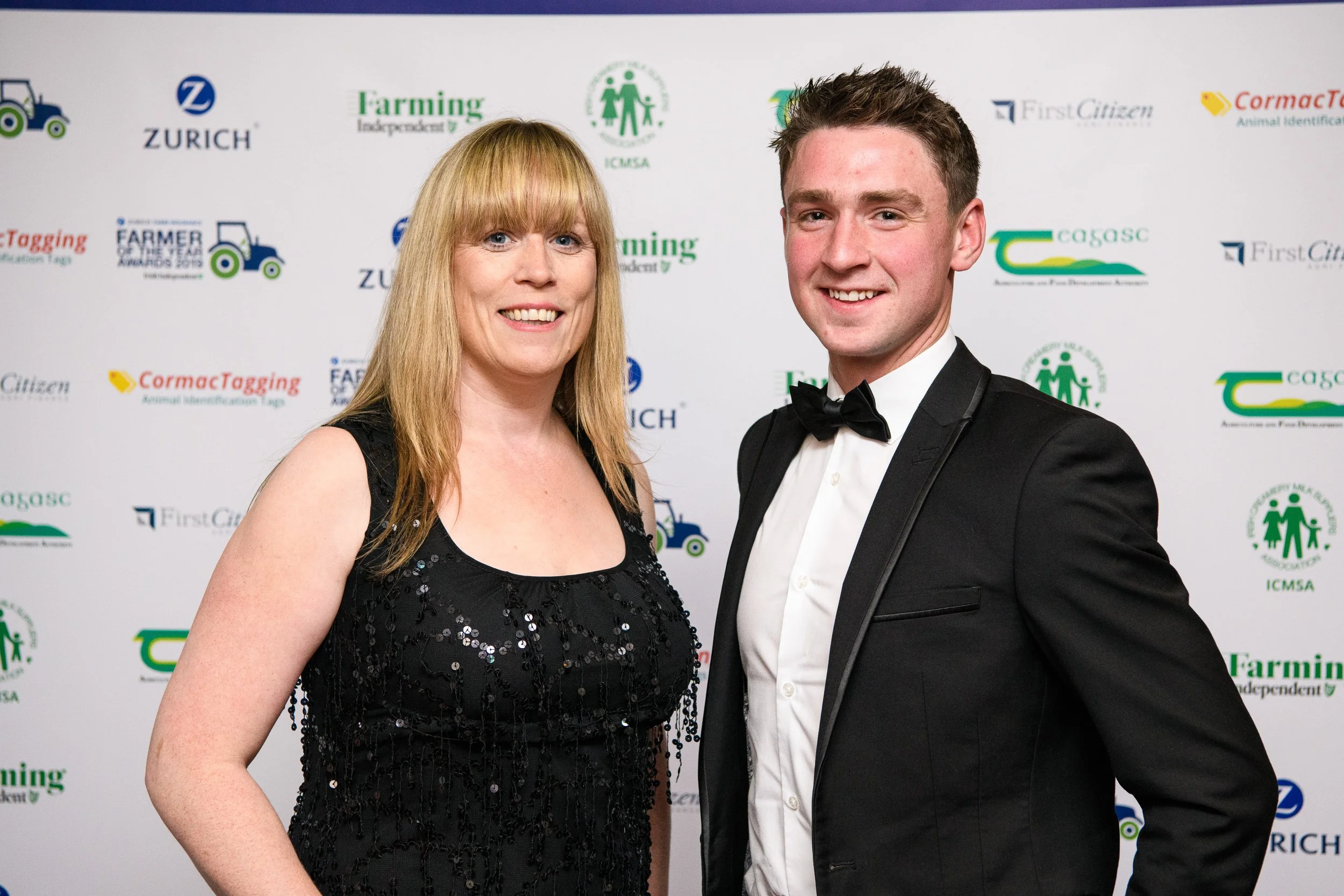 A woman and a man in formal attire posing together at an event, with a backdrop featuring logos and text related to farming and agriculture organizations.
