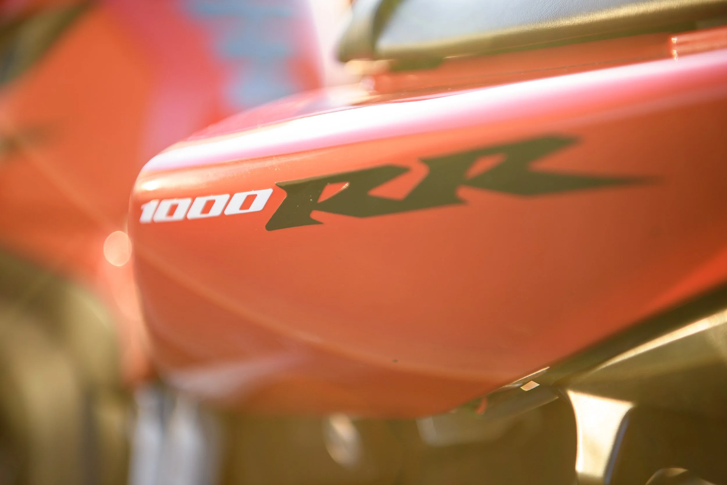 Close-up detail of an orange motorcycle fuel tank featuring ‘1000 RR’ branding decals.

