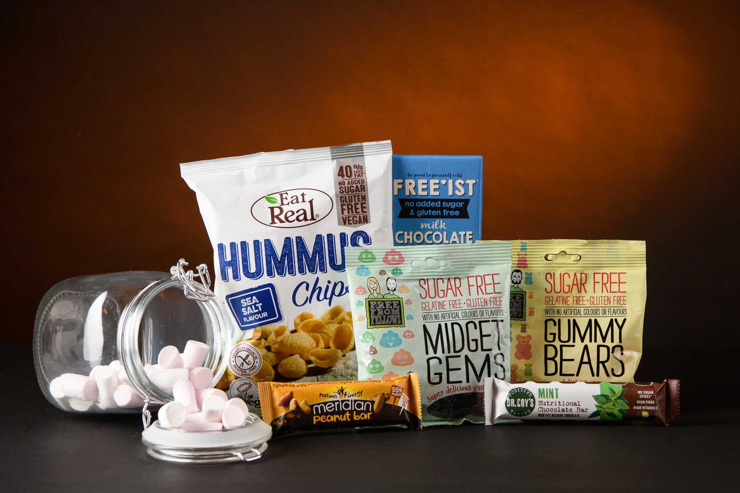 A selection of allergen-free snacks including cereal, sweets, chocolate, and marshmallows presented in a clean product arrangement.

