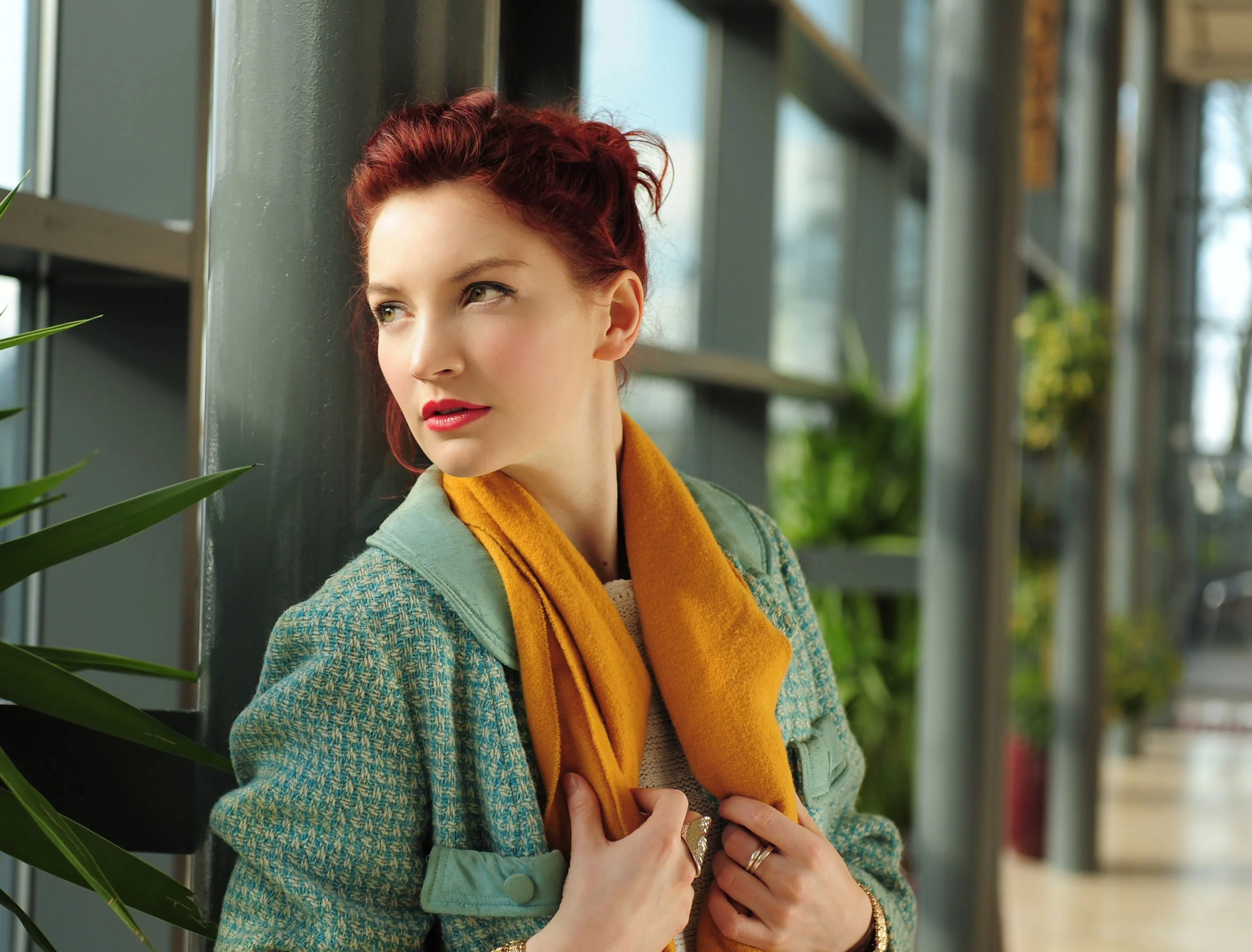 Portrait of a woman leaning against a stone wall wearing a knit sweater and layered outfit
