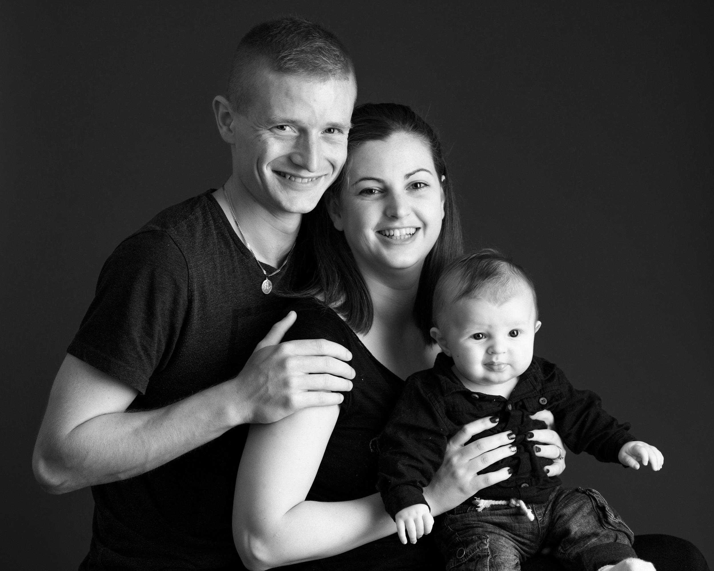 Black and white portrait of a smiling family of three with their baby.
