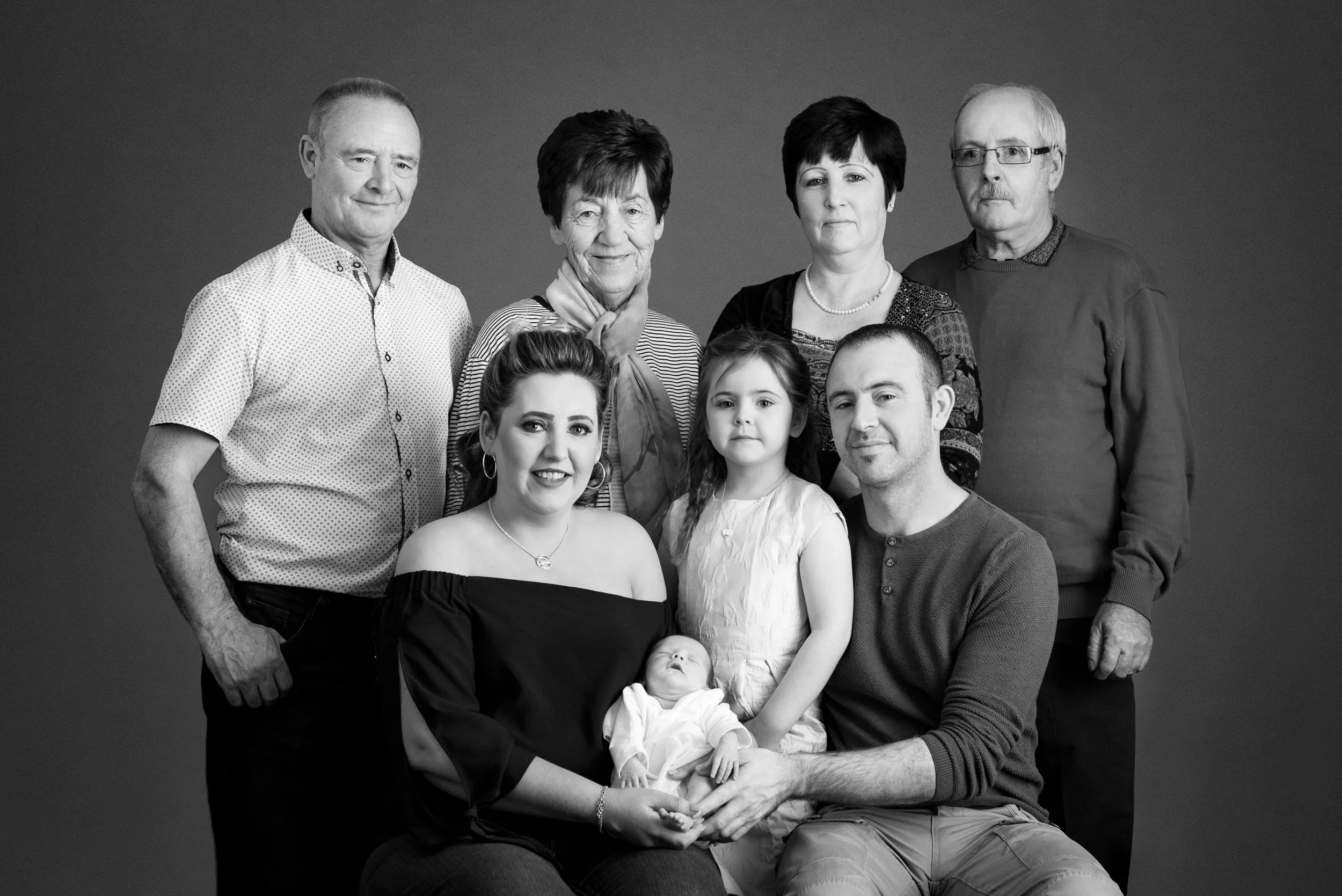 Black and white portrait of a large extended family of nine spanning three generations.
