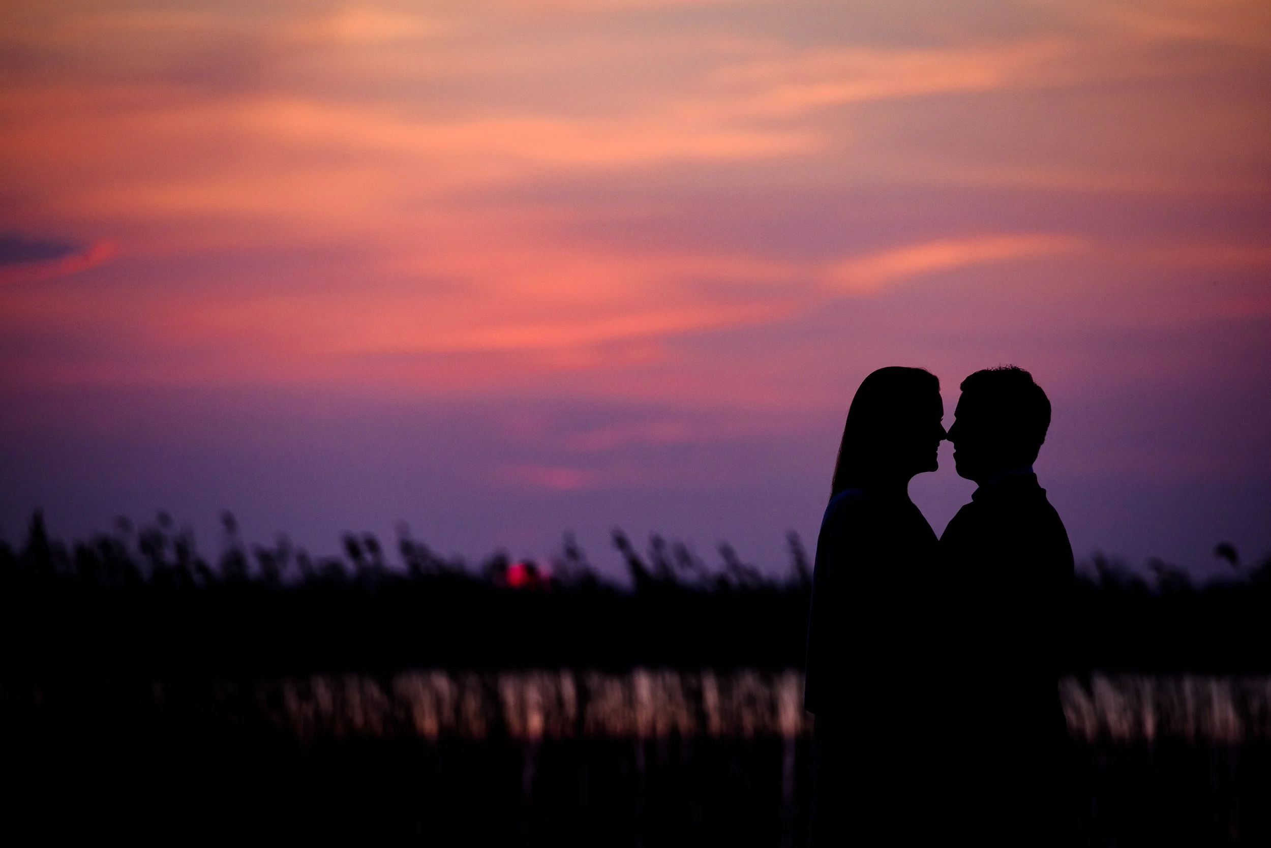 Silhouette of a couple facing each other closely during sunset or twilight, with a colorful sky in shades of pink, purple, and orange, and a dark landscape with tall grass in the background at the Bloomfield House Hotel 