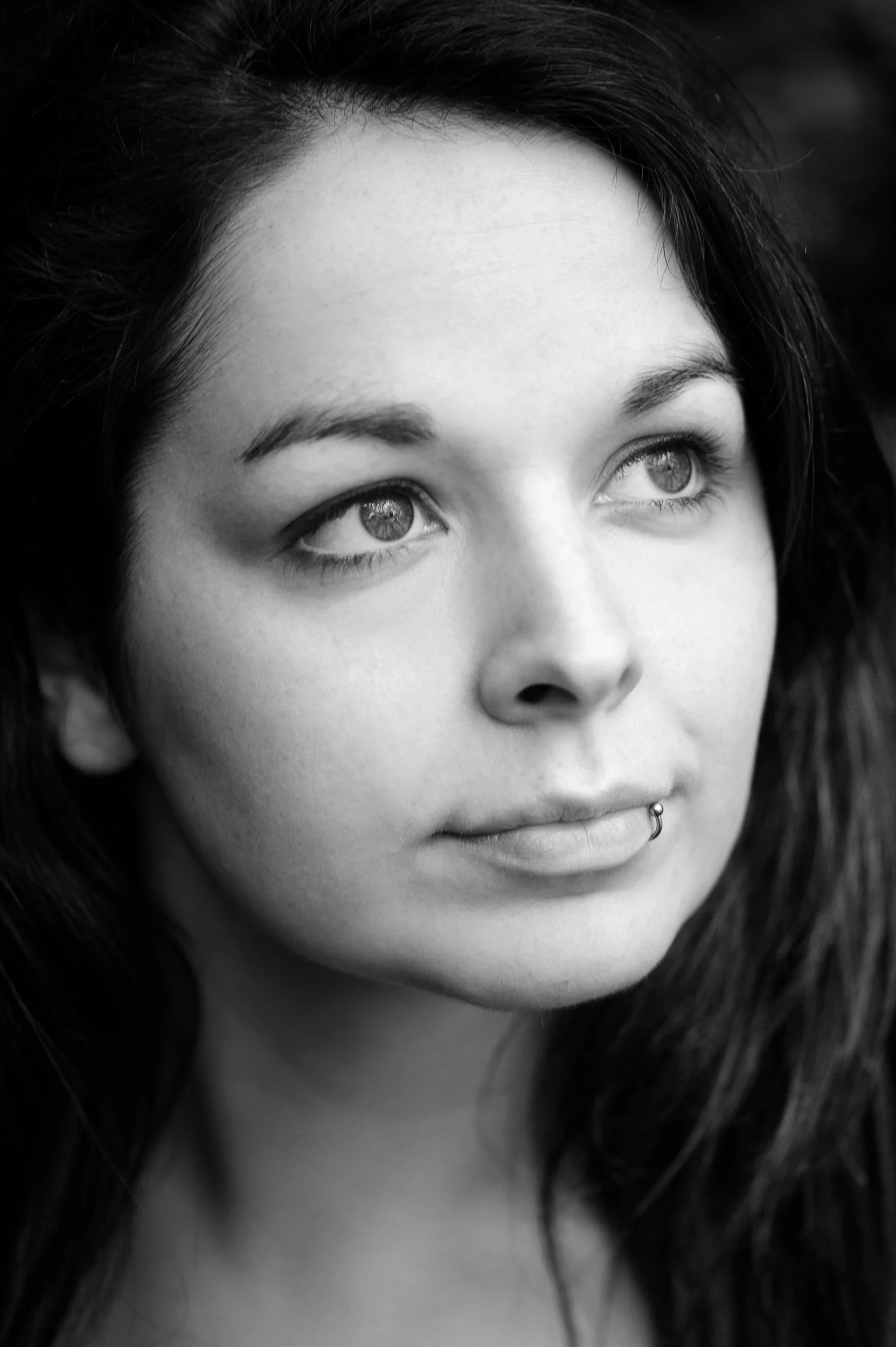 Black and white portrait of a woman with long dark hair and piercing gaze in soft natural light