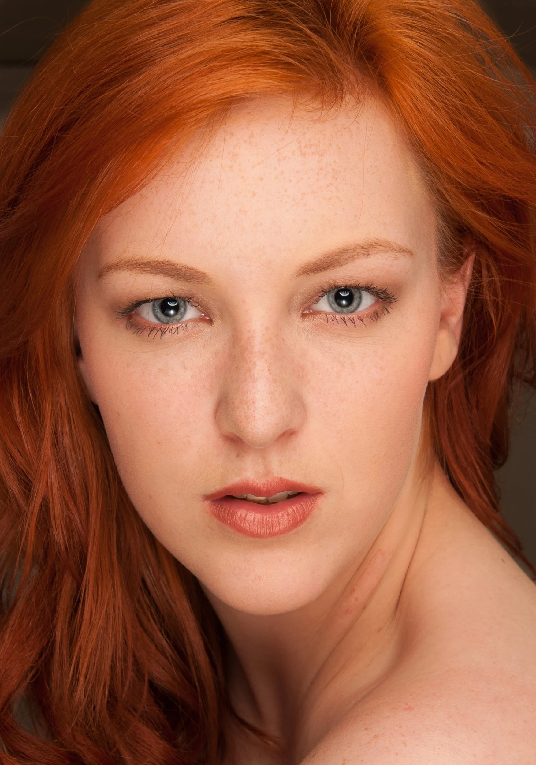 Close-up portrait of a woman with red hair and blue eyes looking directly at the camera
