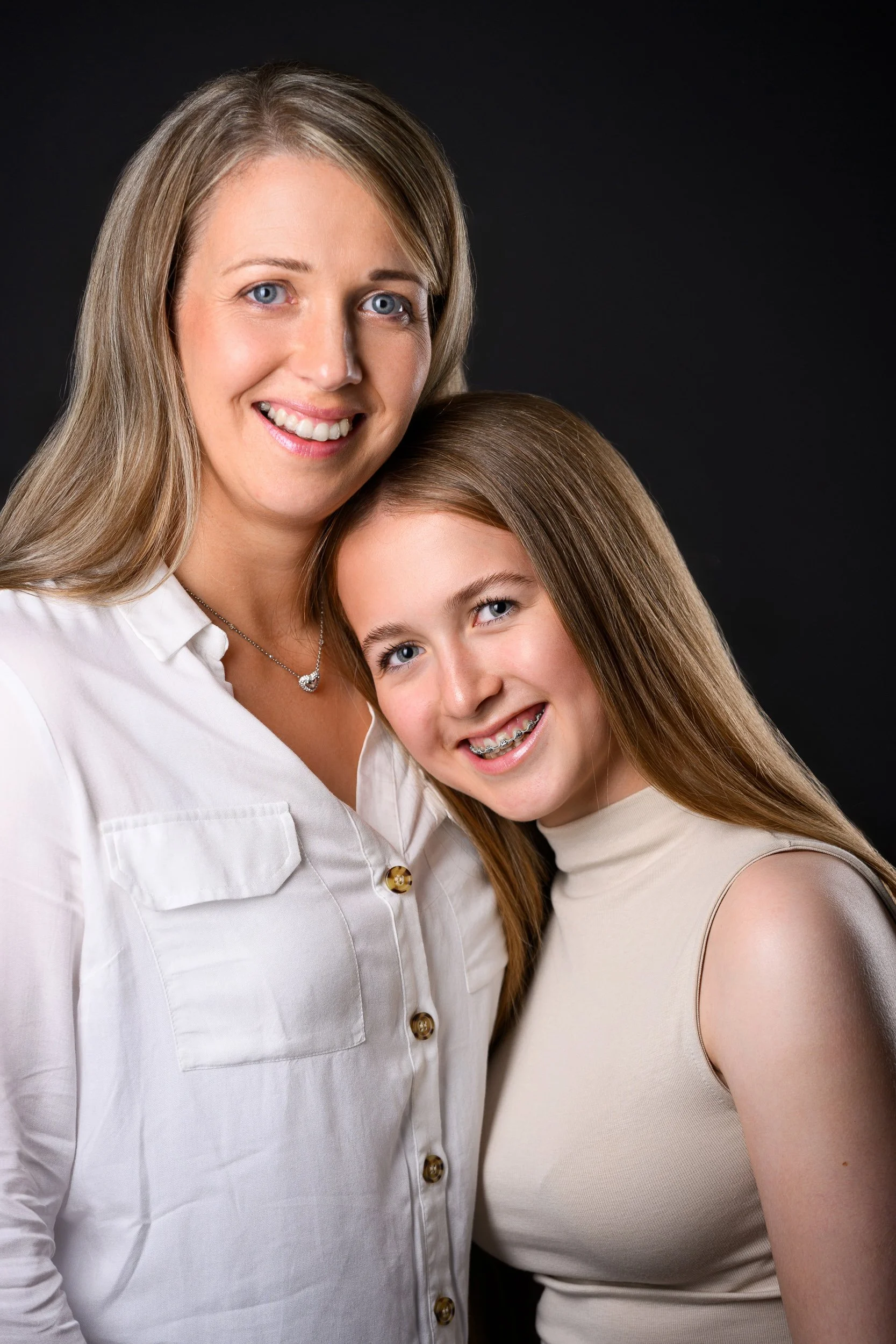 A woman and a teenage girl smiling and posing together against a dark background.