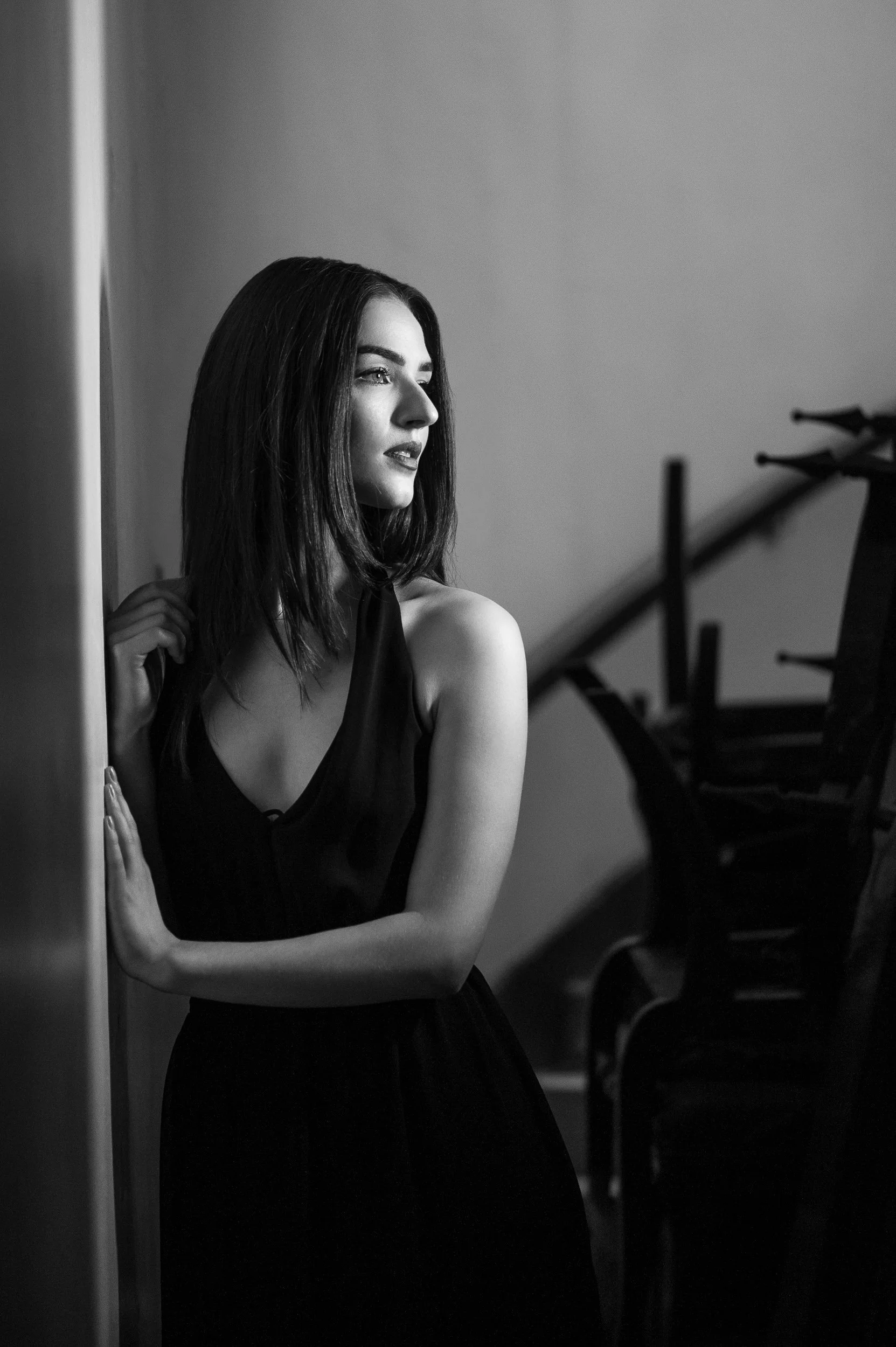 Black and white portrait of a woman with shoulder-length hair standing beside a wall in soft directional light
