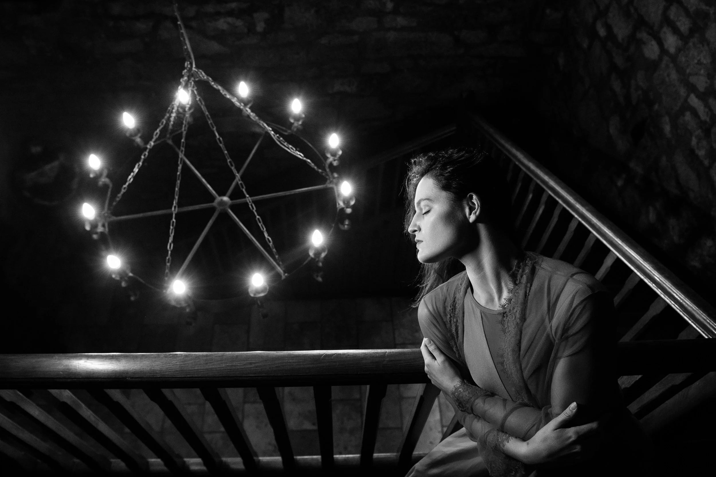 Fine Art Portrait Photography Galway – woman seated on staircase with chandelier light at Cloghan Castle