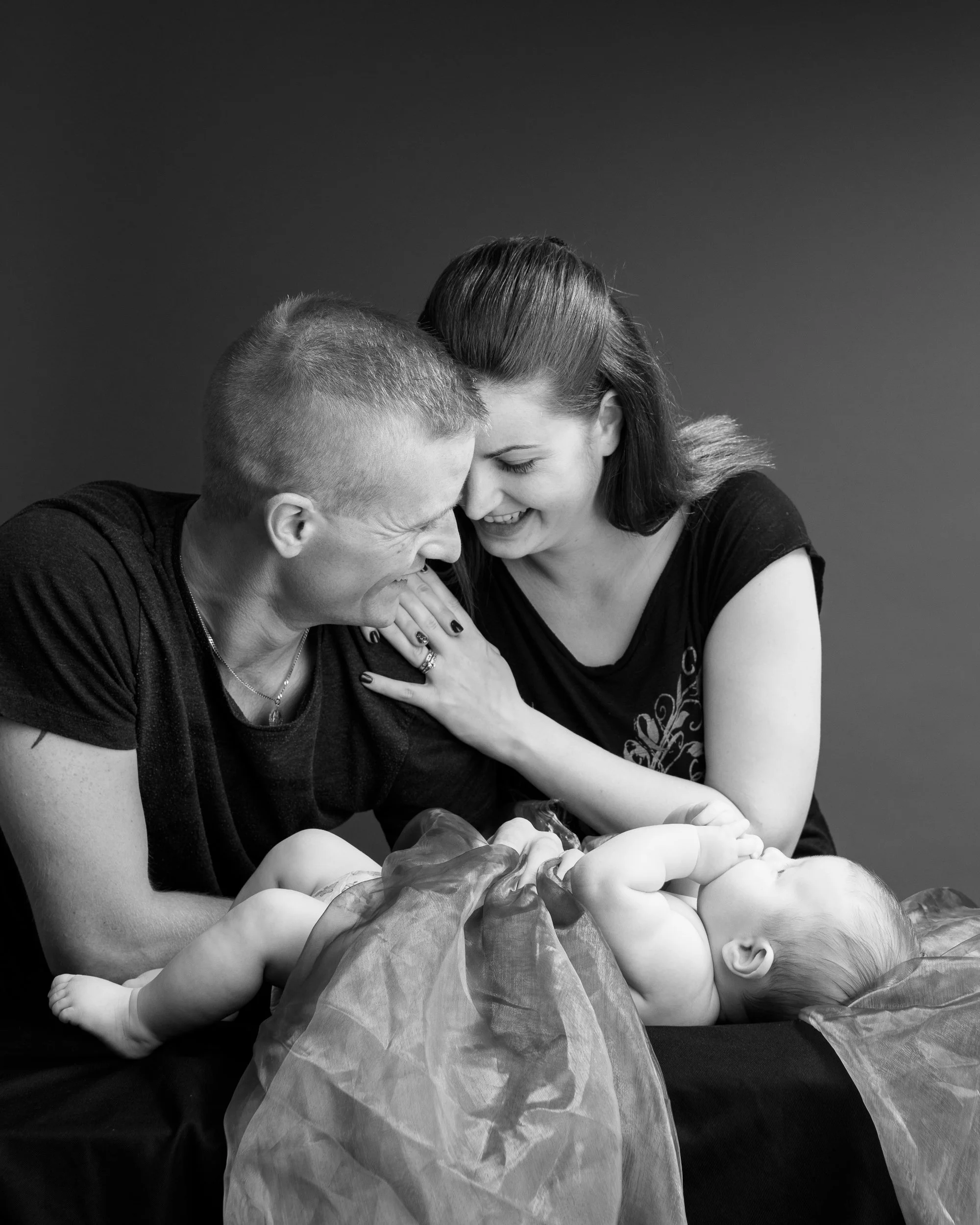 Black and white portrait of a couple celebrating their newborn baby, sharing a joyful moment together.
