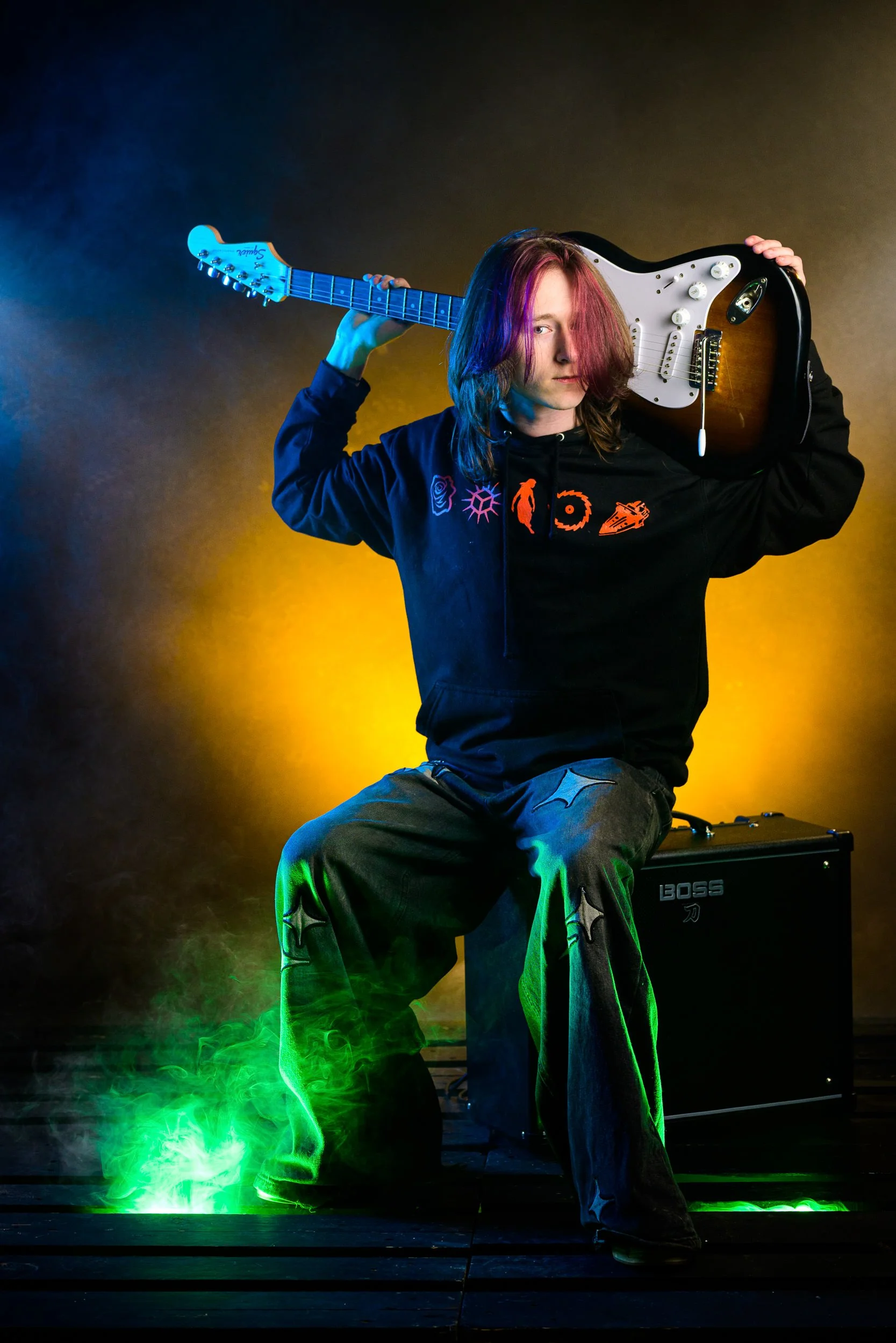 Creative portrait of a musician holding an electric guitar with coloured smoke and gradient lighting
