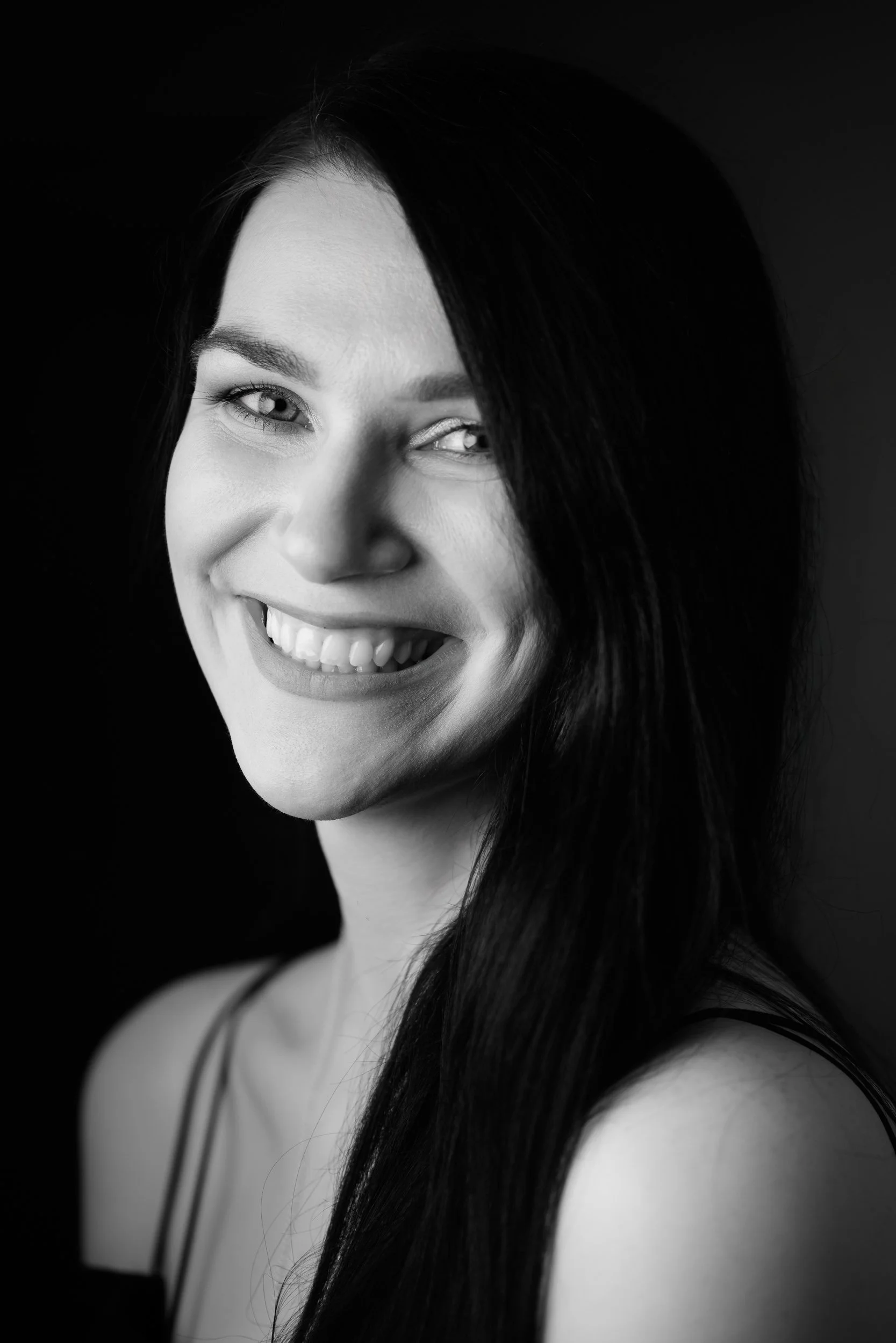 Black and white portrait of a smiling woman with long dark hair in soft light
