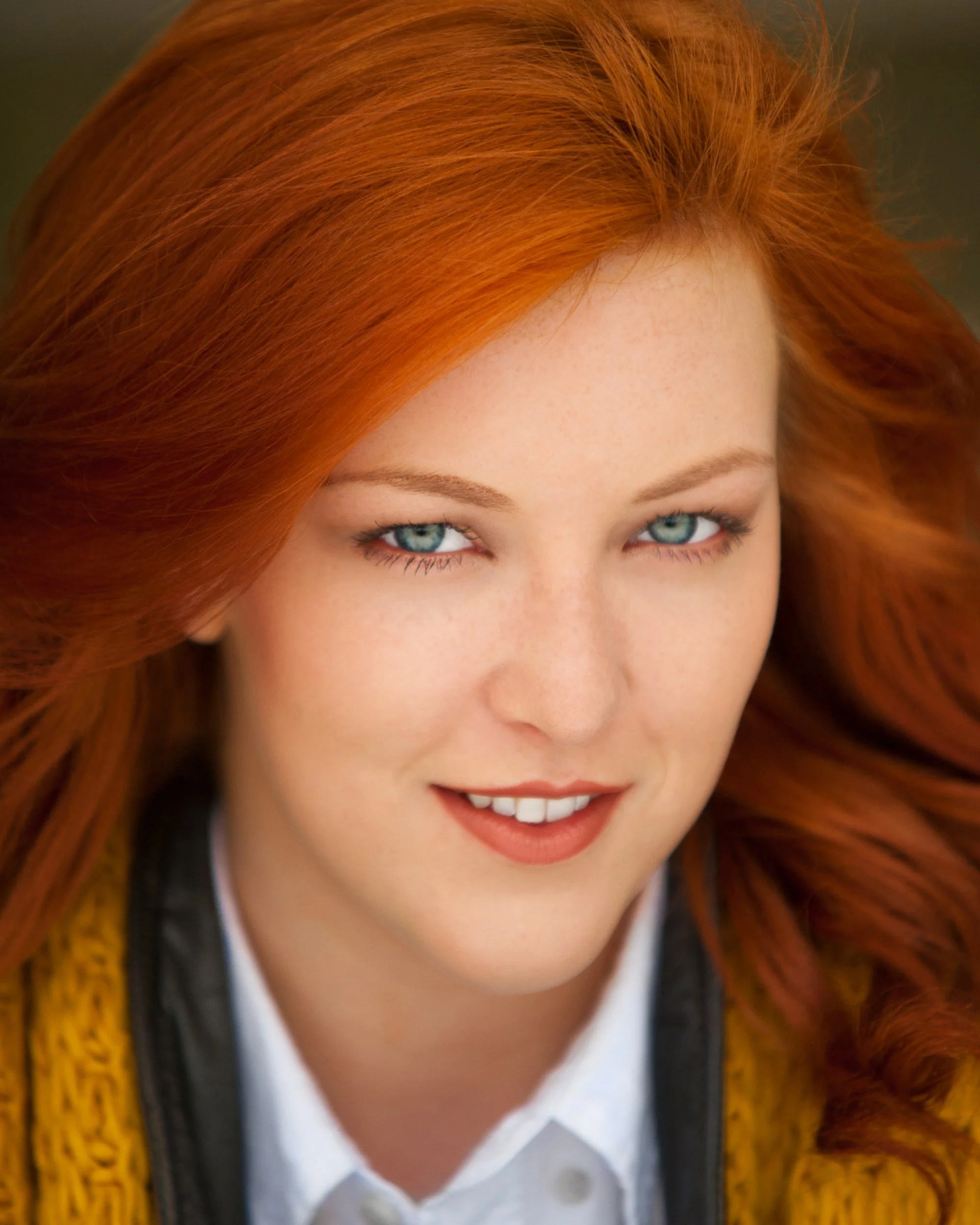 Close-up portrait of a woman with long red hair and blue eyes in soft natural light
