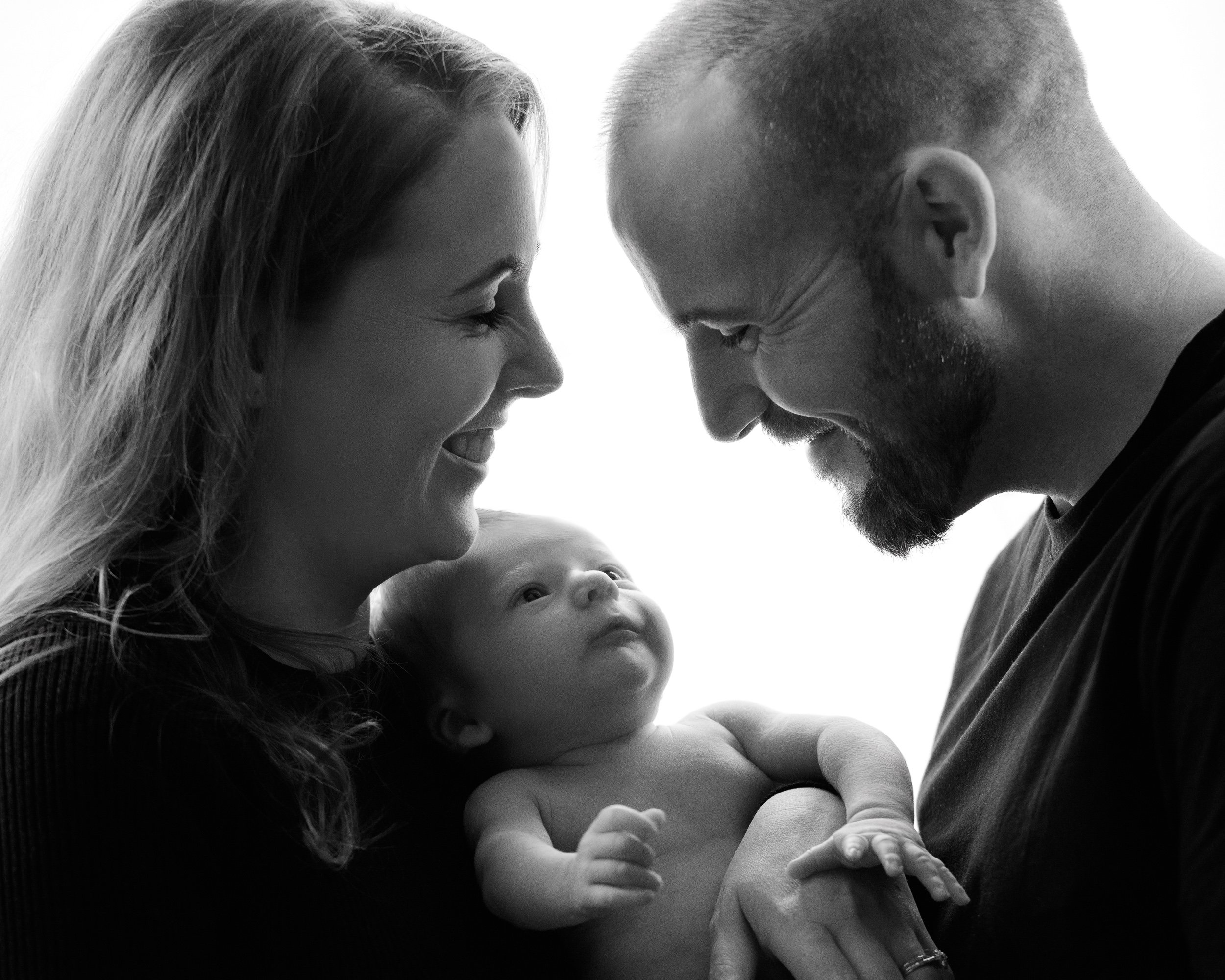 Black and white family portrait of parents holding their baby, sharing a joyful and intimate moment together.
