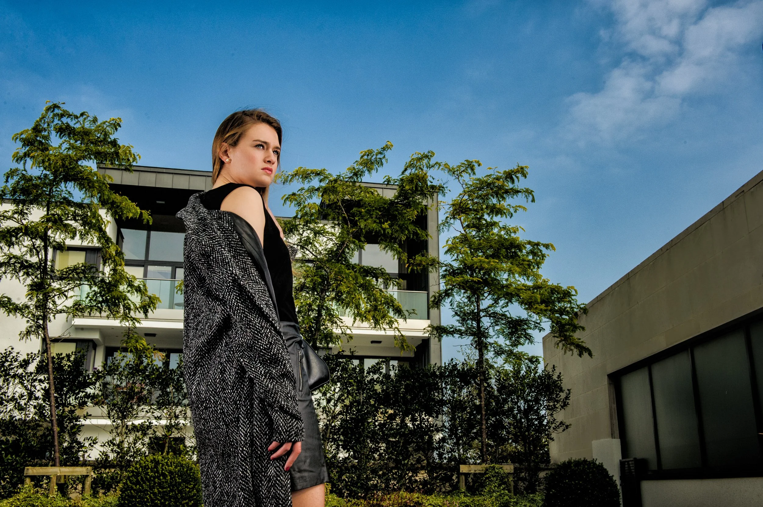 Urban portrait of a woman in a leather skirt and coat standing confidently in front of modern buildings at the Sheraton hotel athlone 
