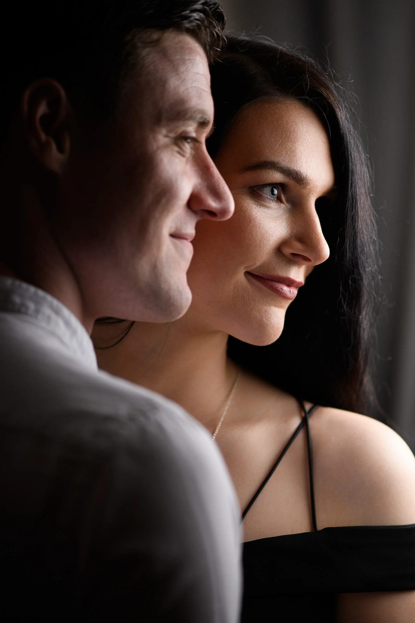 Close-up couple portrait of a smiling man and woman looking out a window, side profile.
