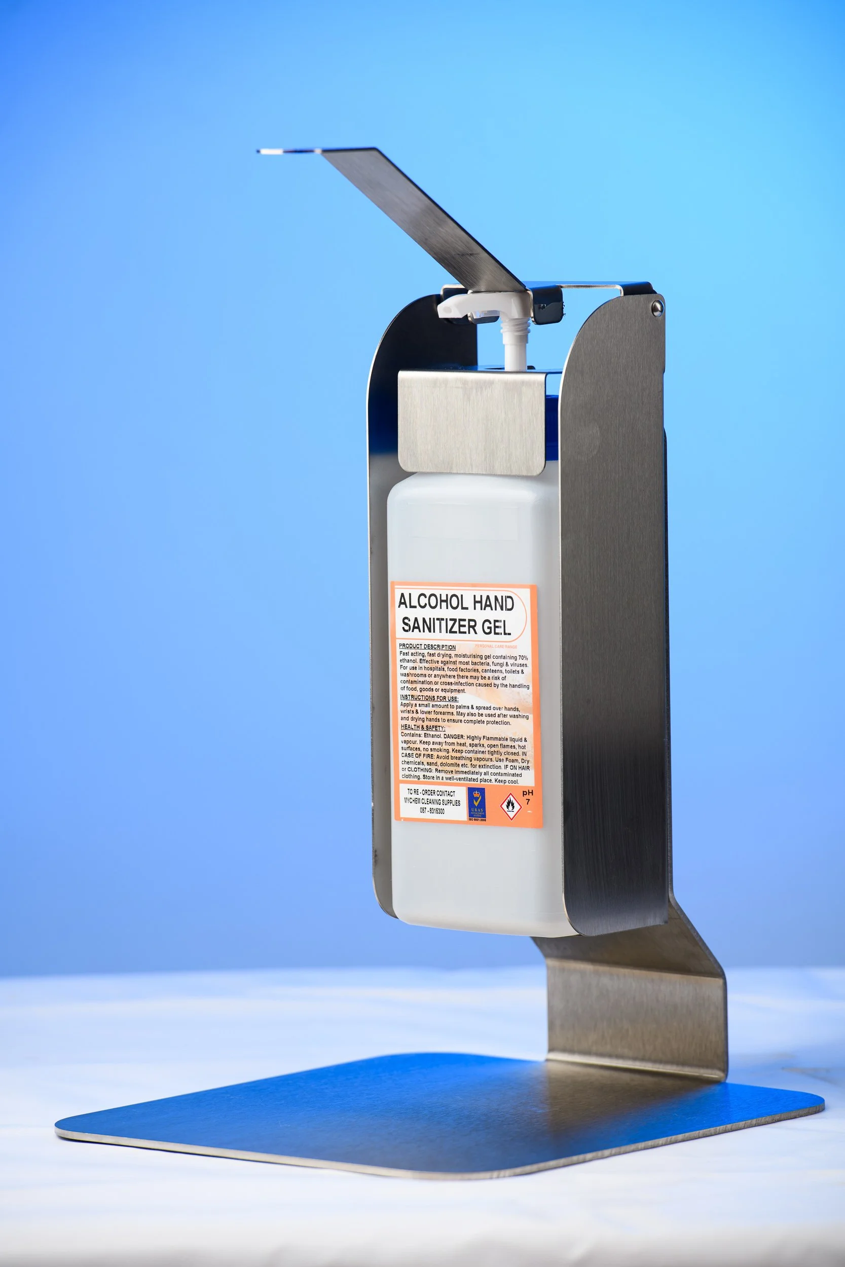 Wall-mounted hand sanitiser dispenser filled with gel, photographed against a blue background.
