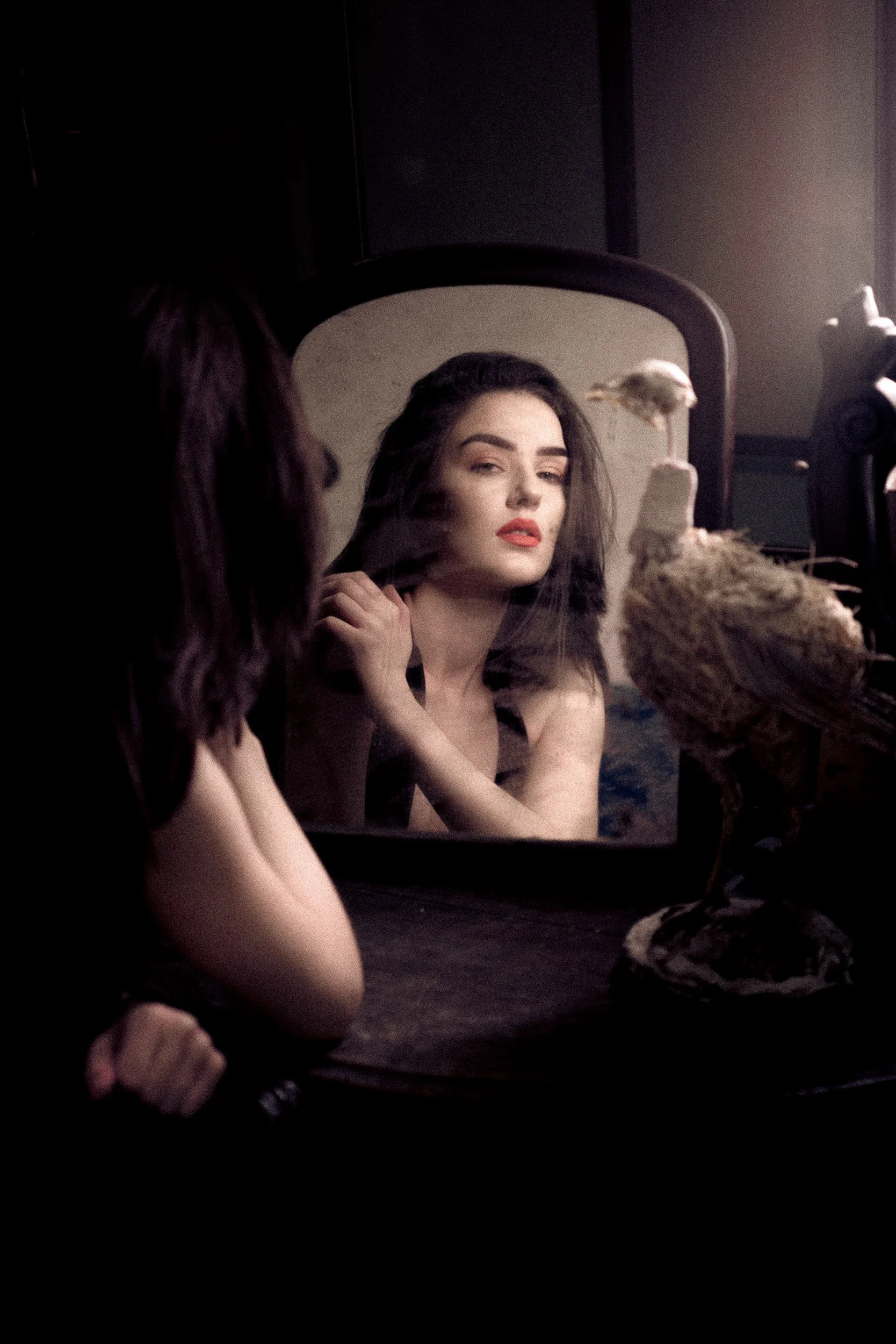Artistic mirror portrait of a woman with red lipstick surrounded by makeup and decorative objects
