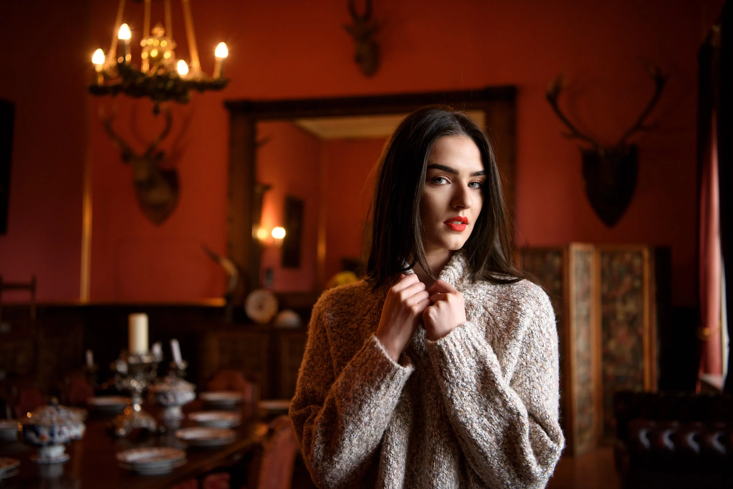 Creative portrait in Ardgilan Castle of a woman with dark hair and red lipstick in a vintage-style room with chandelier and wall decor
