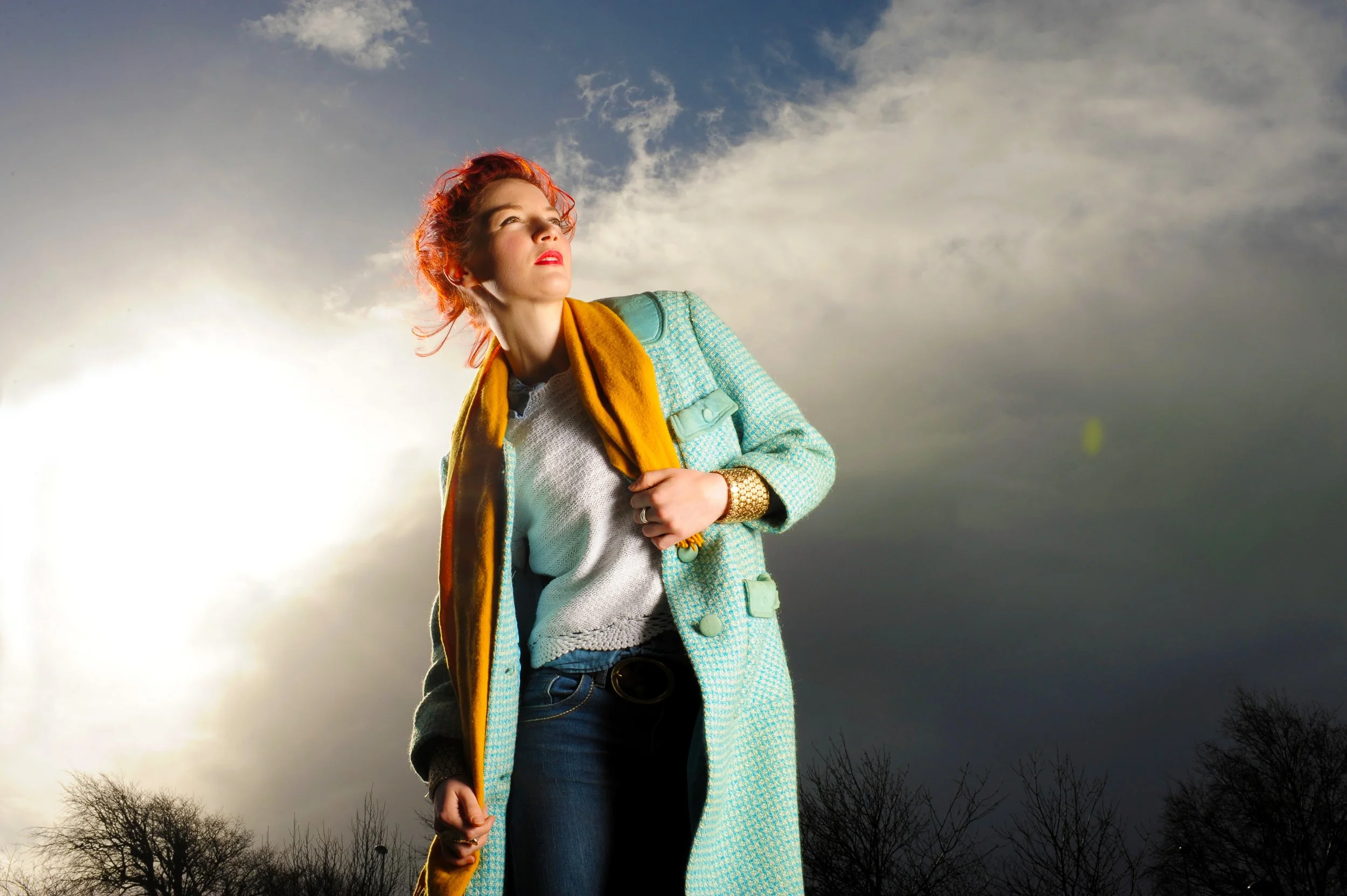 Outdoor portrait of a woman in a blue coat and scarf standing under a cloudy sky
