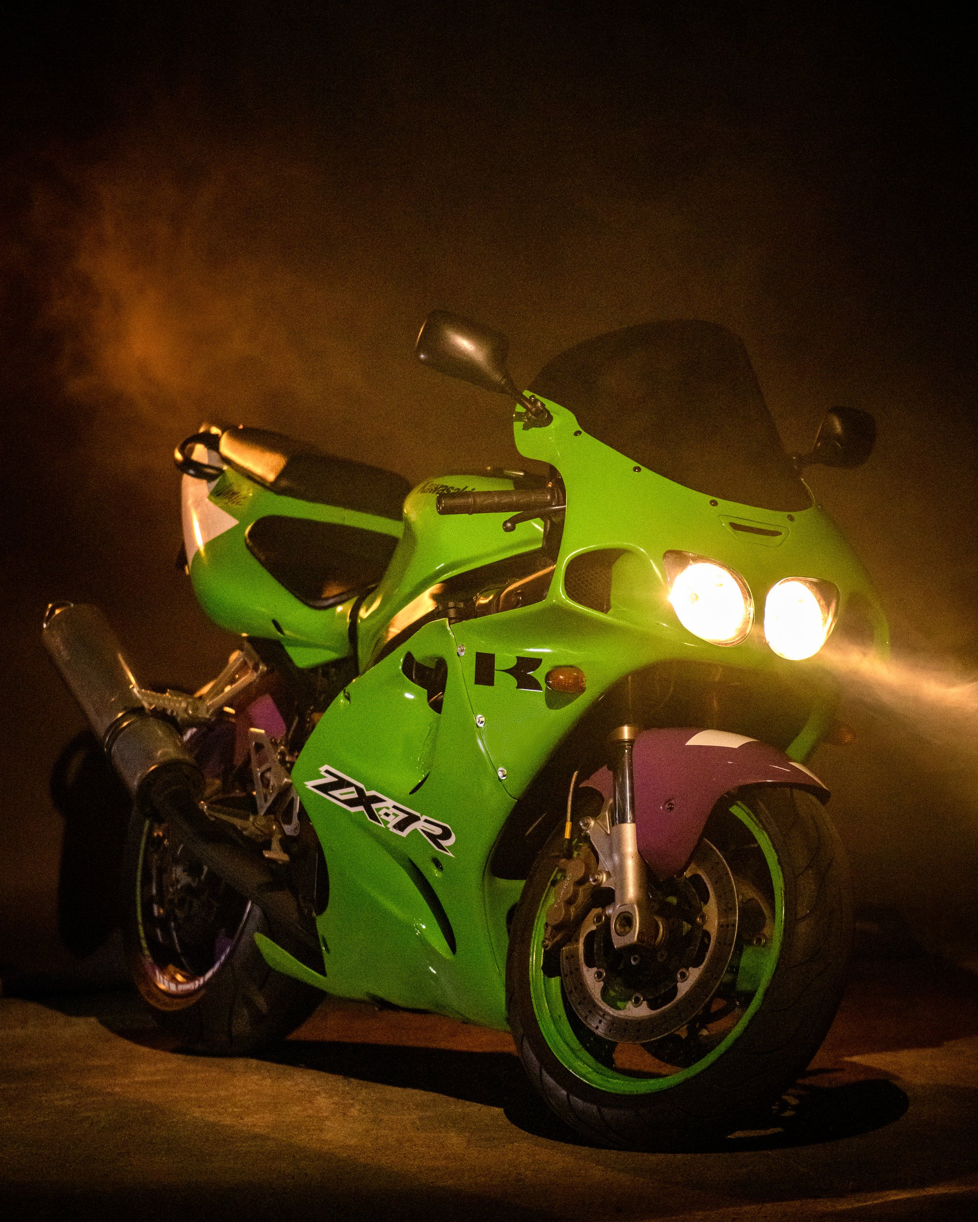 Kawasaki ZX-7R in green with headlights on, photographed in a dark setting.