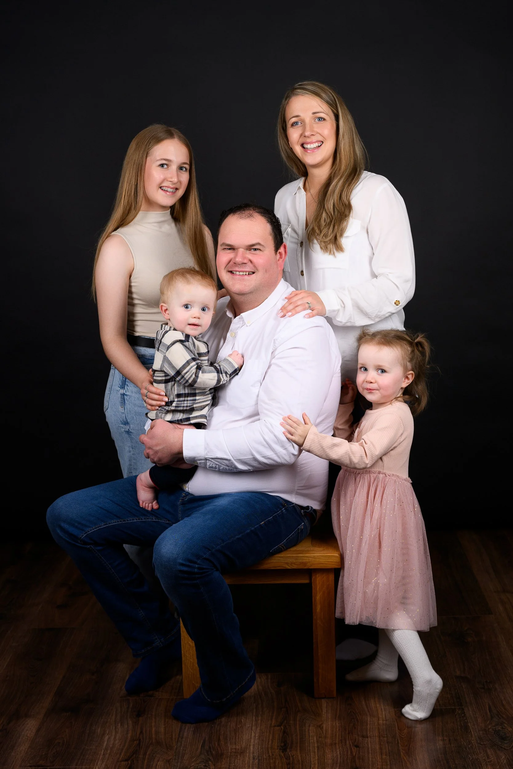 Family portrait of five members including parents and three children, posed together against a black background.
