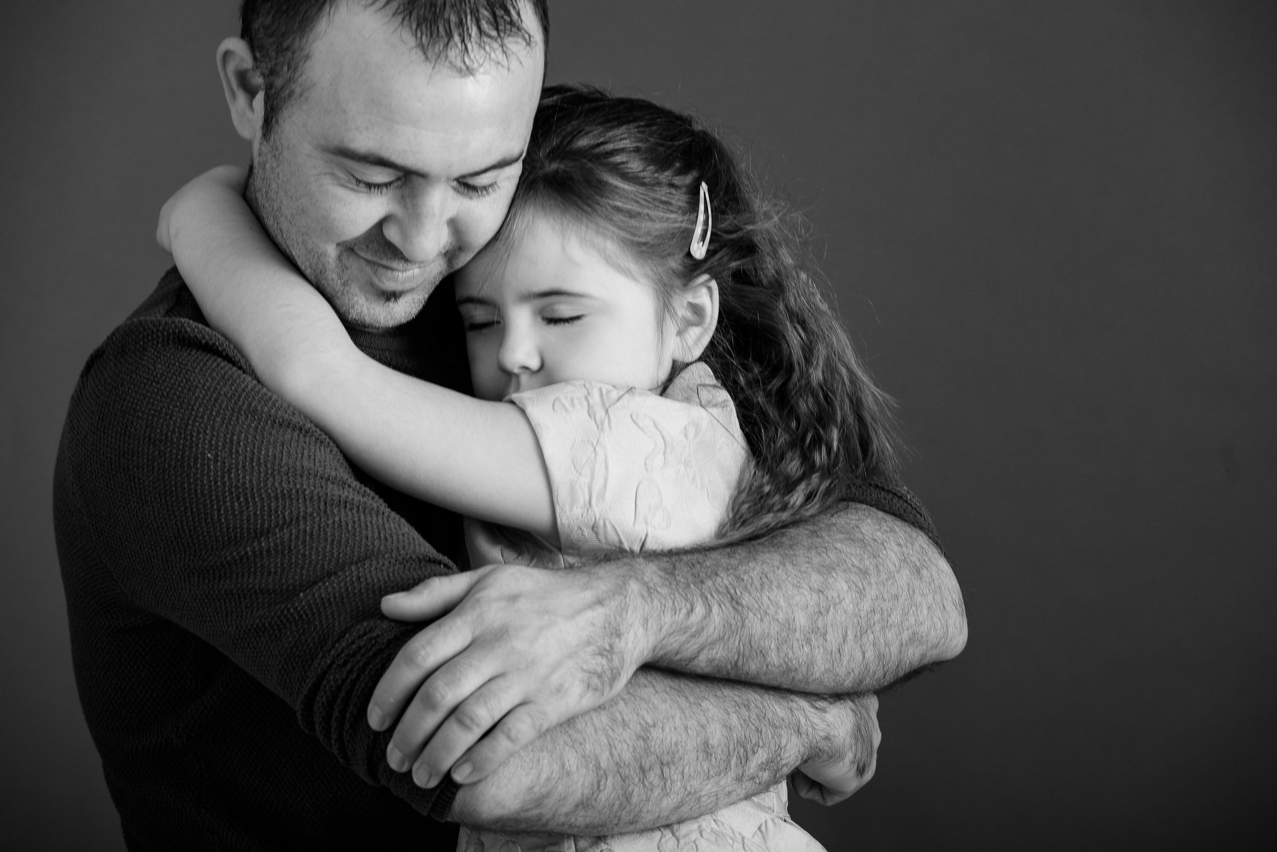 Black and white portrait of a man hugging a young girl, both with peaceful expressions and closed eyes.
