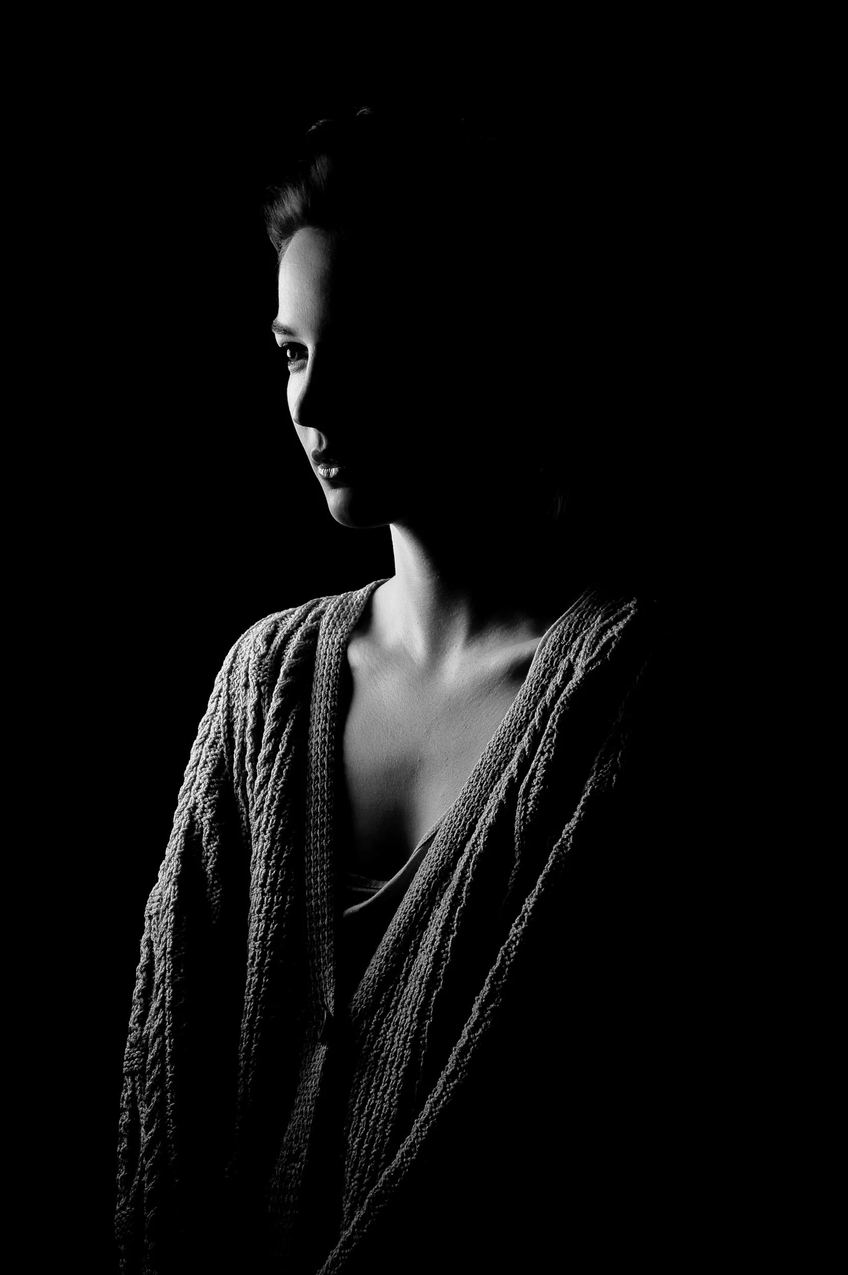 Black and white portrait of a woman in dramatic lighting with textured clothing against a dark background