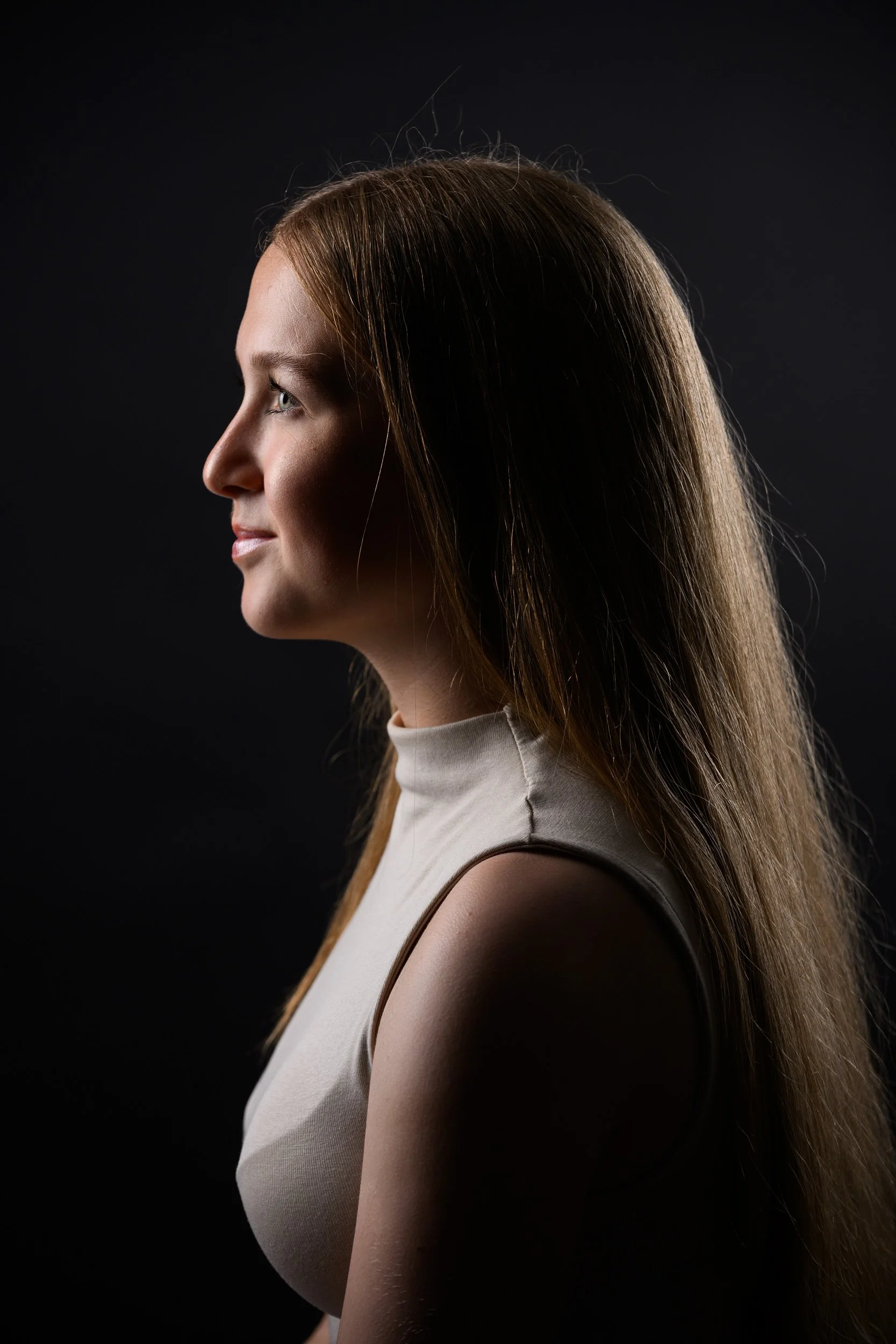 Profile portrait of a young woman with long auburn hair against a dark background.
