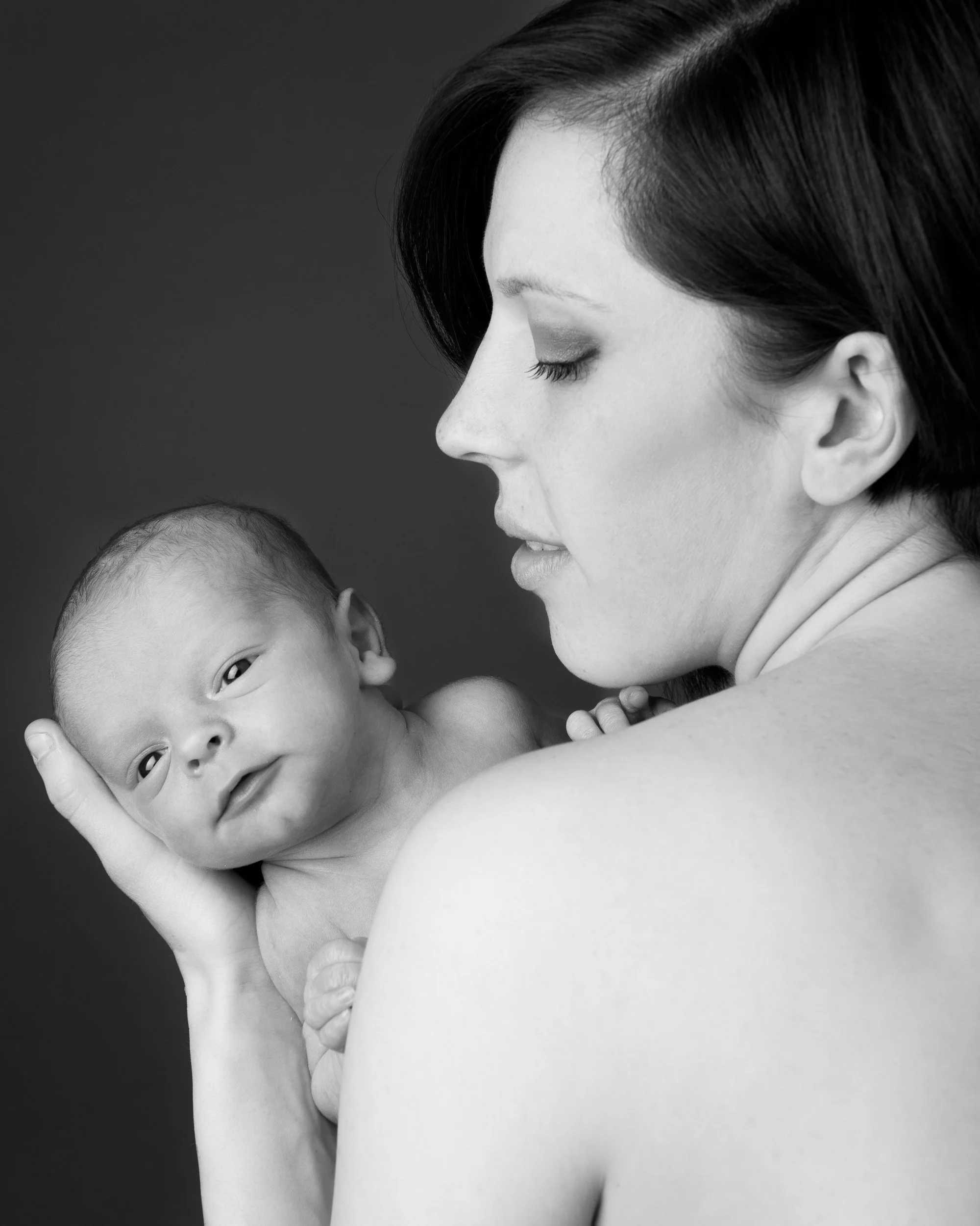 Black and white portrait of a woman holding a newborn baby, with the baby looking towards the camera.
