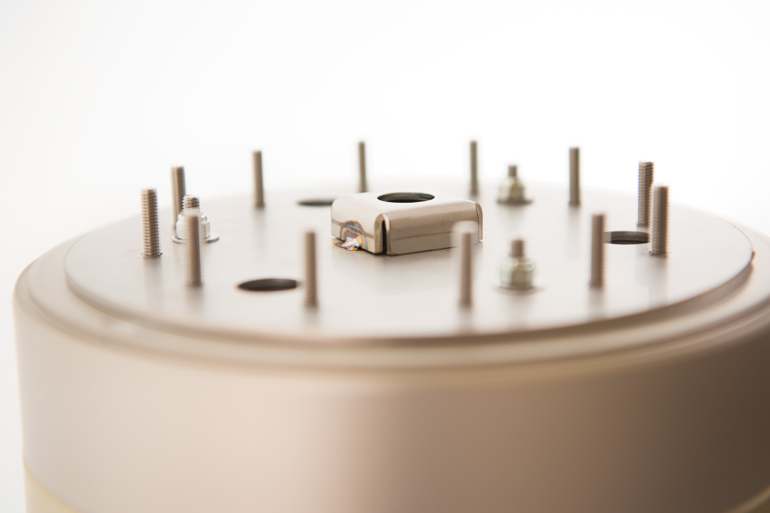 Close-up of a scientific or industrial device with multiple metal screws and a central metallic component on a white surface.