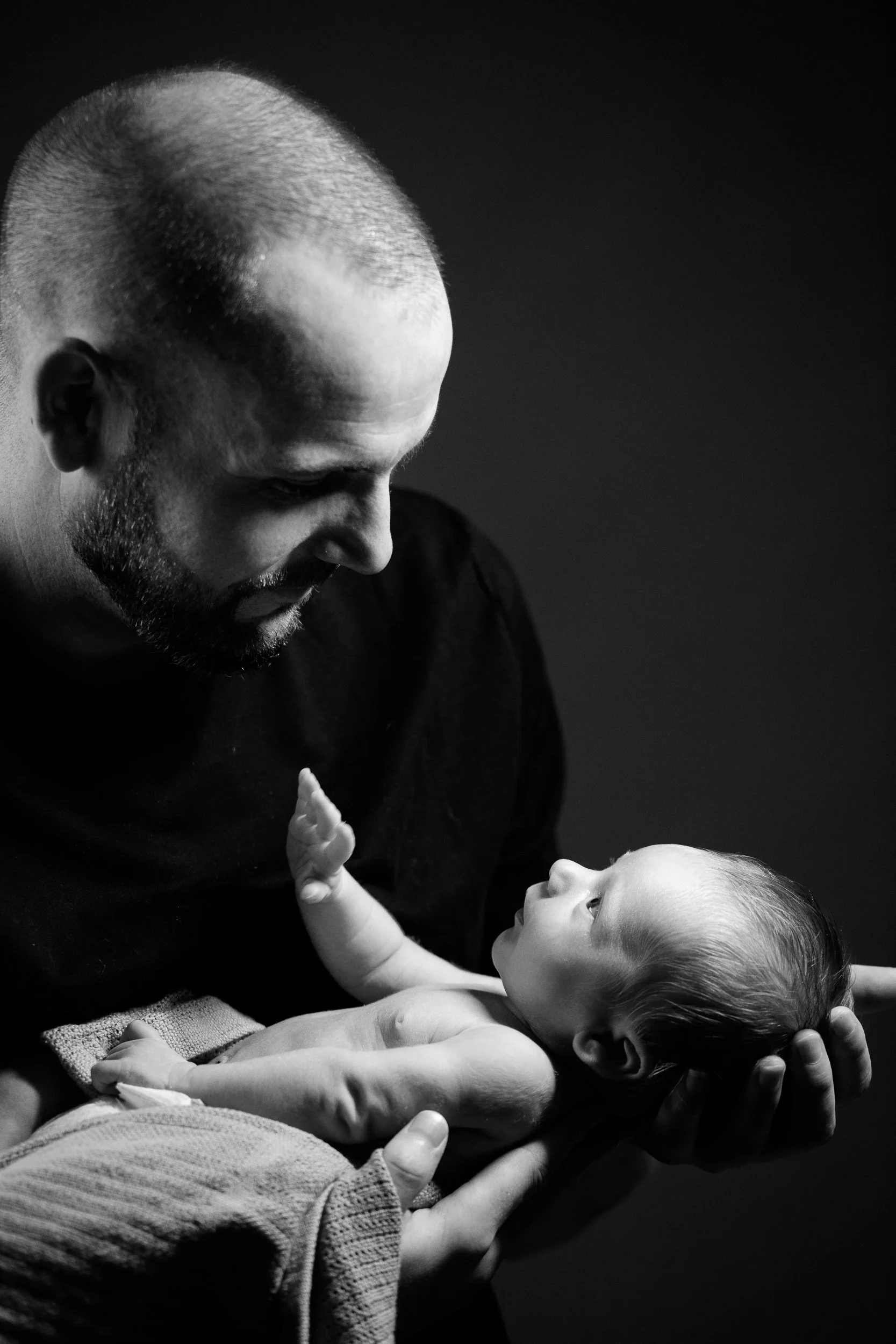 Black and white portrait of a man gently holding a newborn baby in his hands, looking down with care.
