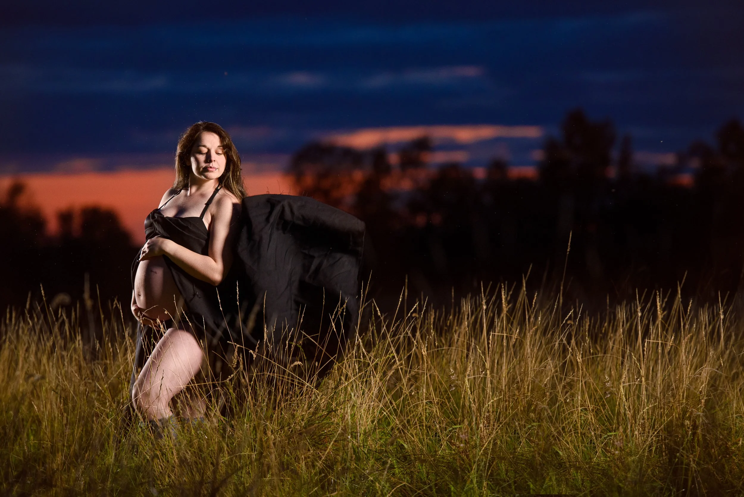 Ken Byrne Photography - Maternity shoot in a field at sunset wearing a black wrap, with a warm evening sky behind her.
