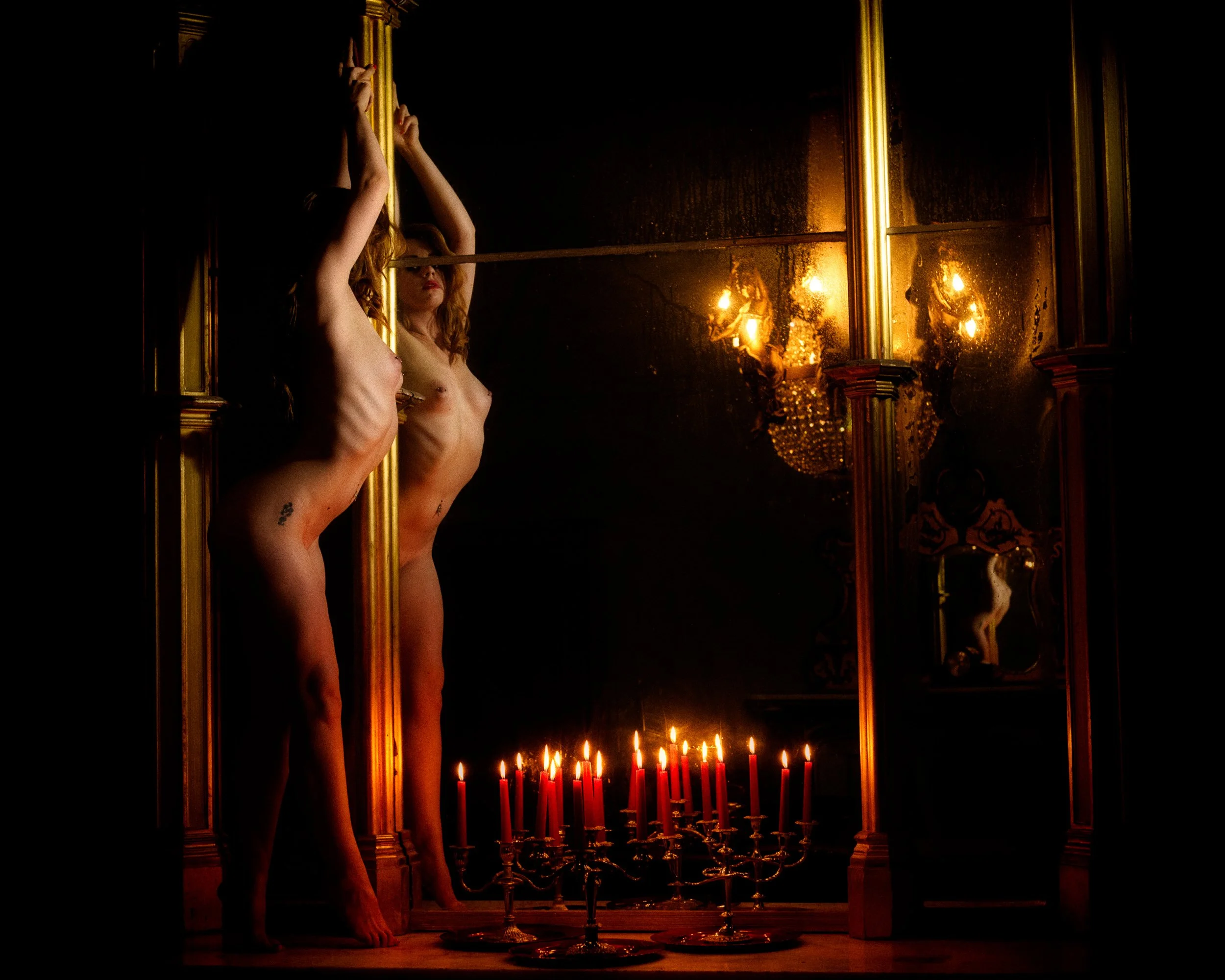A woman with red hair standing before a mirror with candlelight and ornate décor, creating a dramatic and atmospheric scene in Charleville Castle 
