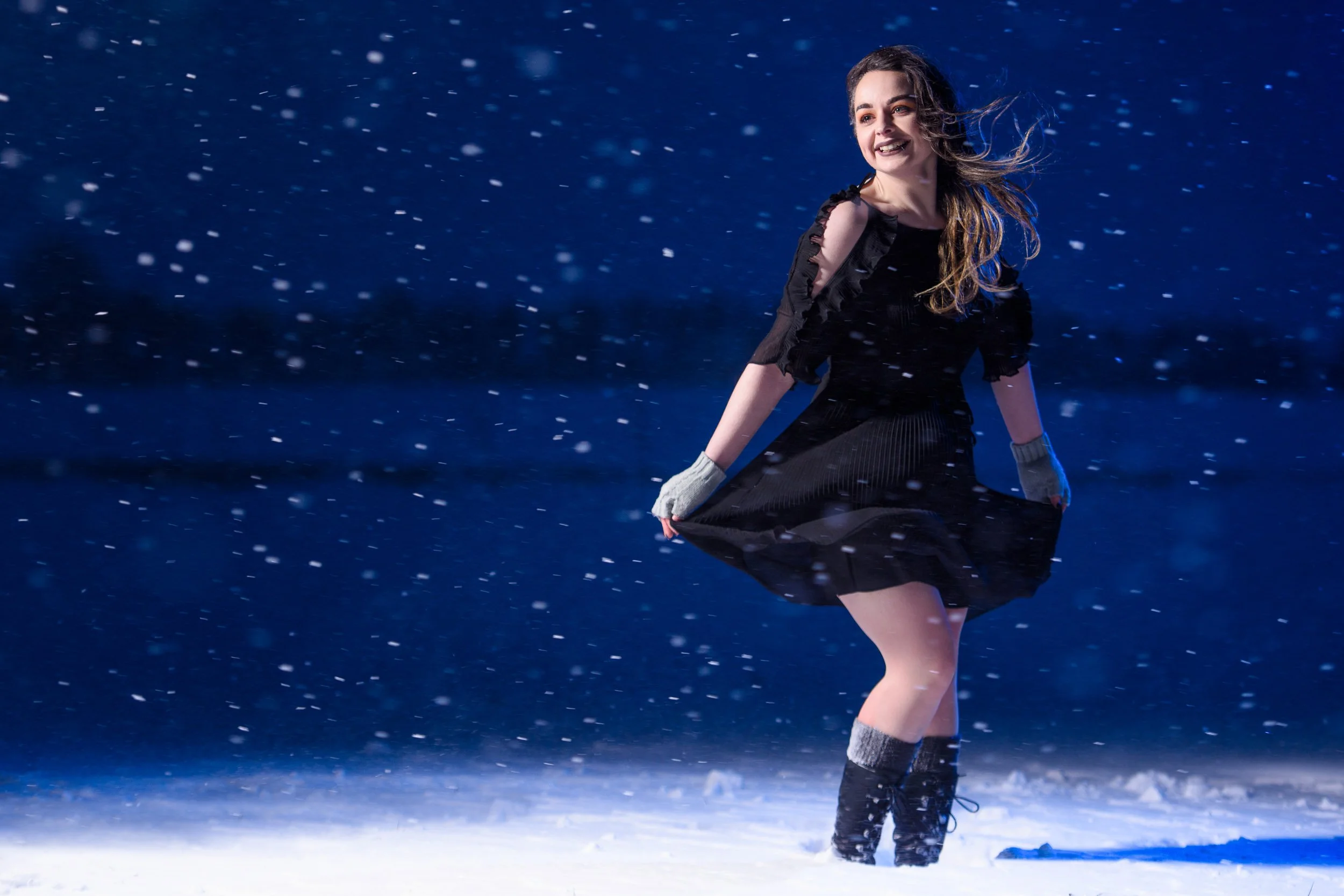 Moody night portrait of a woman in snowfall wearing a black dress and gloves
