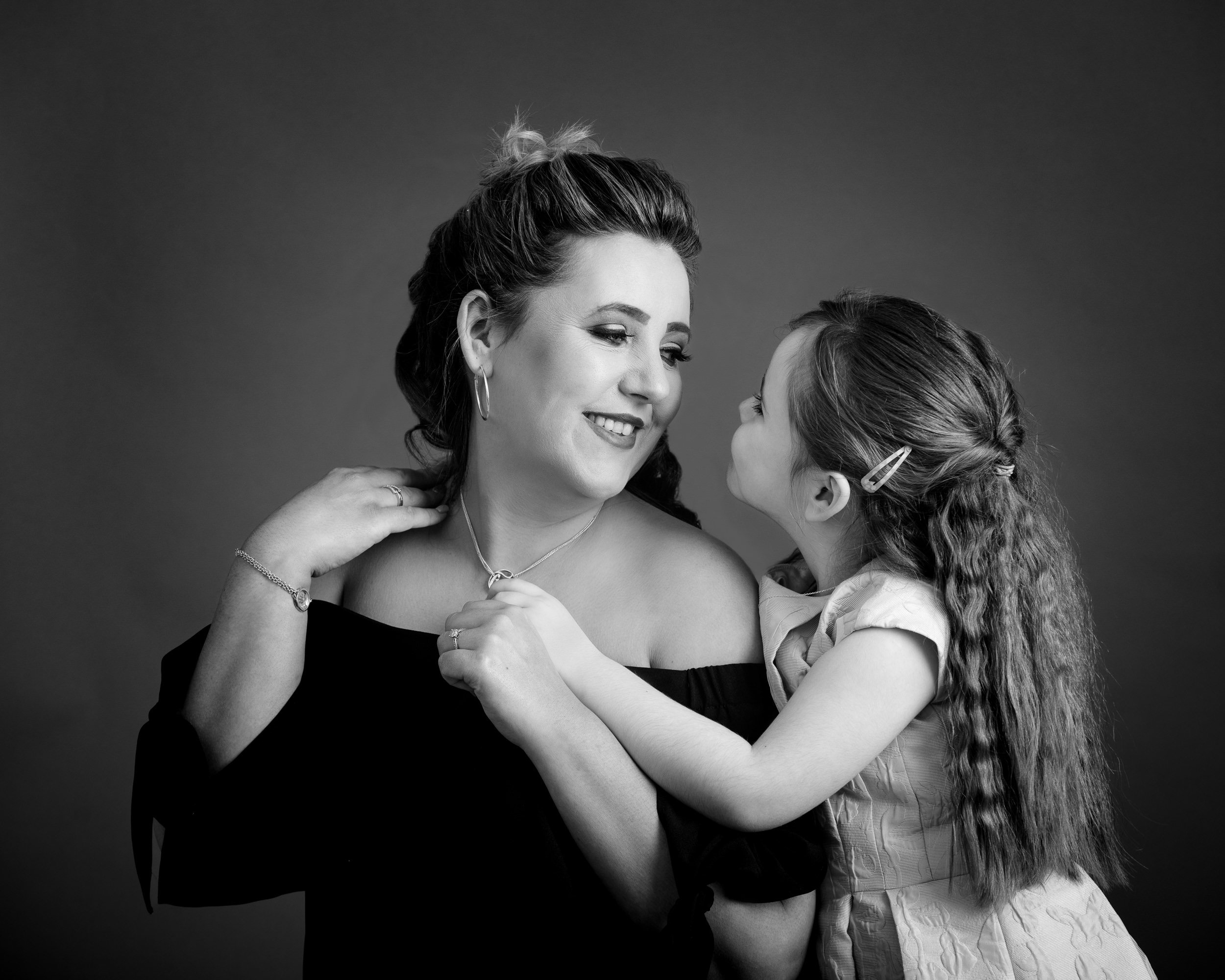 Ken Byrne Portrait Photography Black and white portrait of a woman and young girl sharing a joyful moment, smiling and holding hands.
