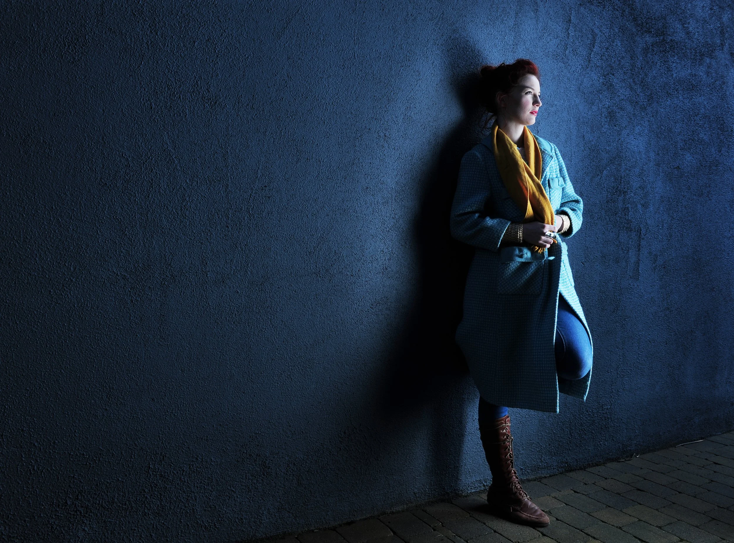 Ken Byrne Photography Portrait Editorial of a red-haired woman in a blue coat and yellow scarf against a dark textured wall
