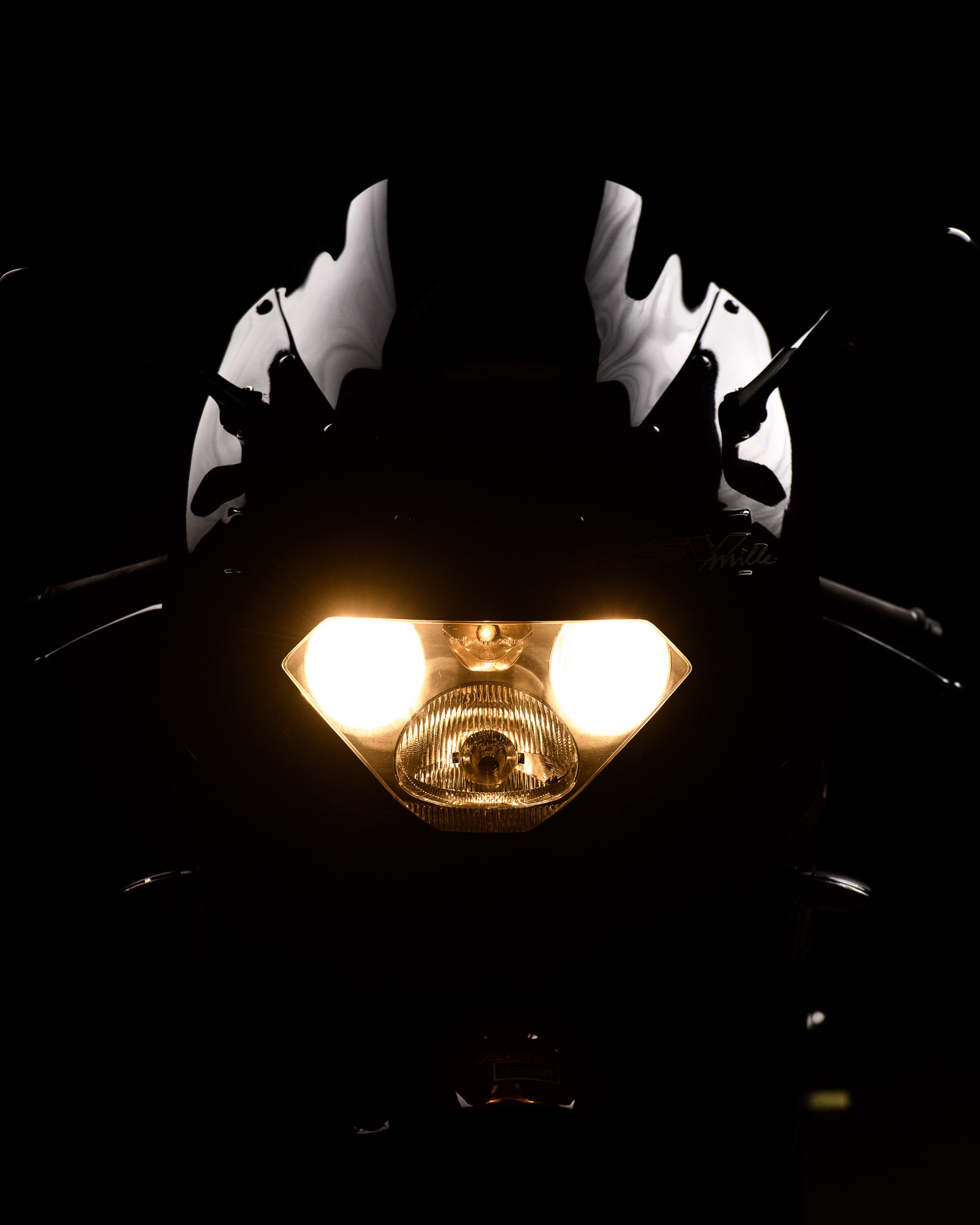 Sport motorcycle with headlights illuminated in a low-light environment, creating a dramatic front-facing composition.
