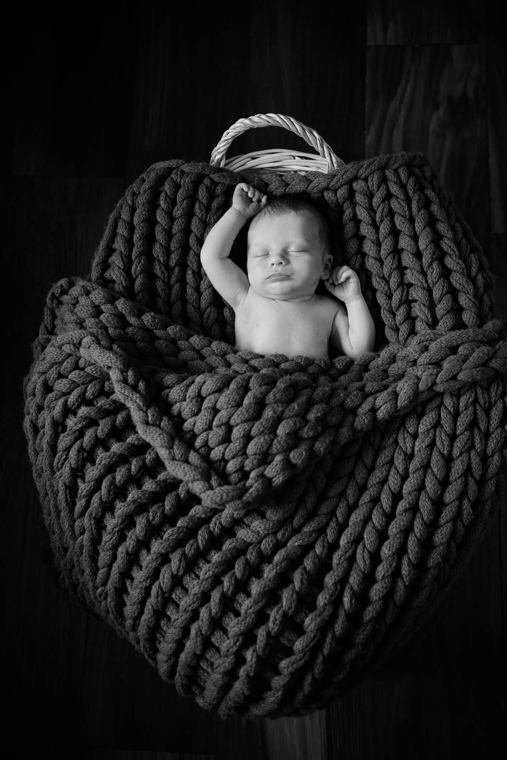 A black and white photo of a sleeping newborn baby lying in a knitted basket.