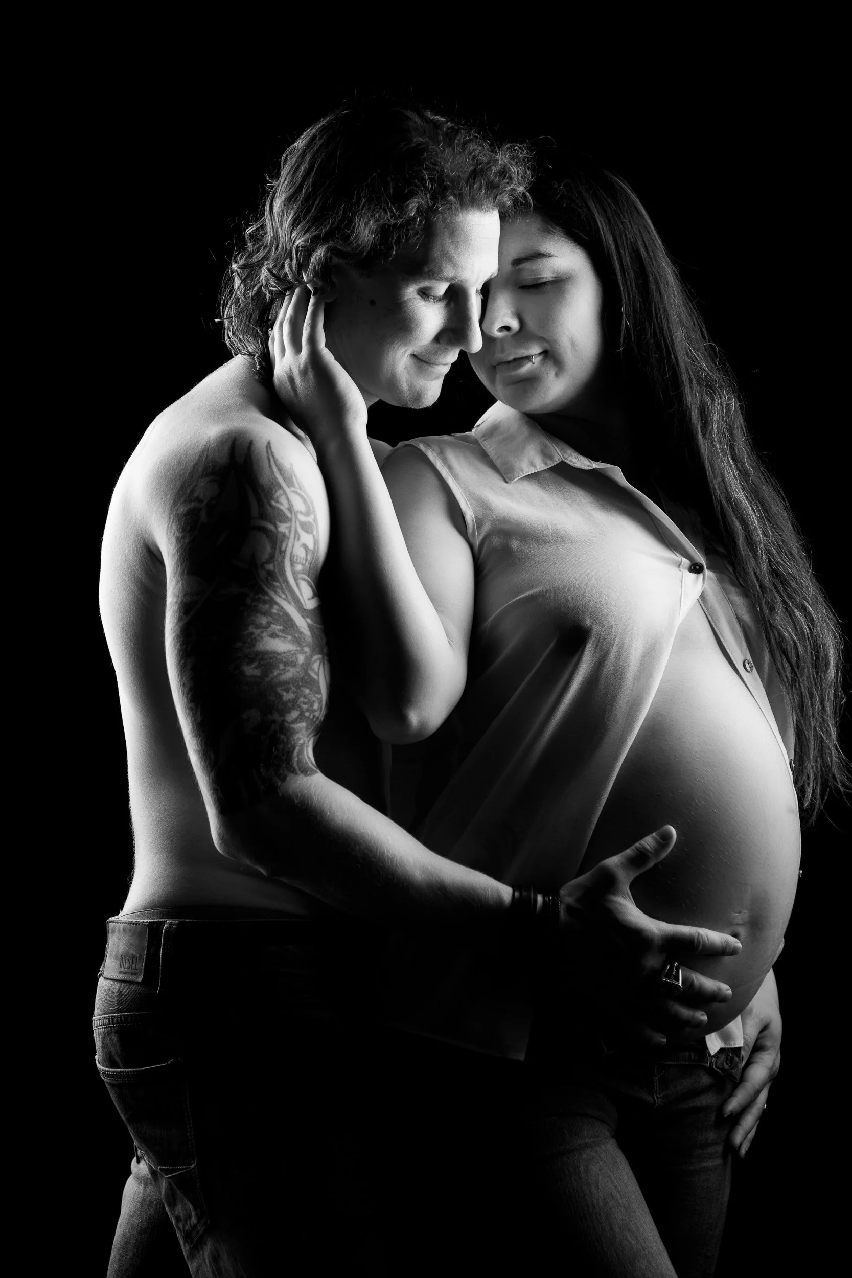 Black and white portrait of a pregnant couple sharing an intimate moment with their foreheads touching.
