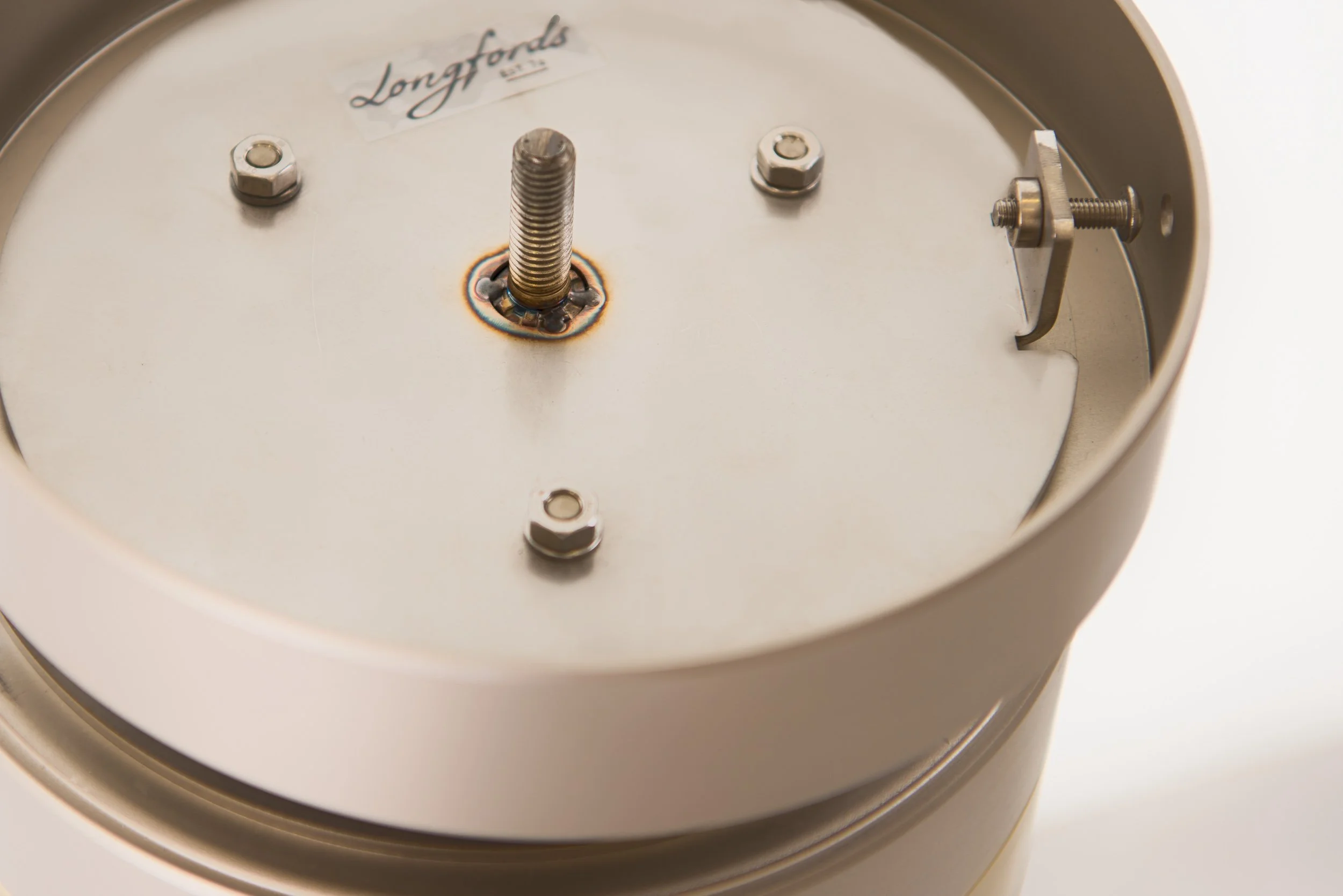 Close-up of a vintage clock face showing the center with the Longfords logo, clock hands not present, and visible mounting hardware.