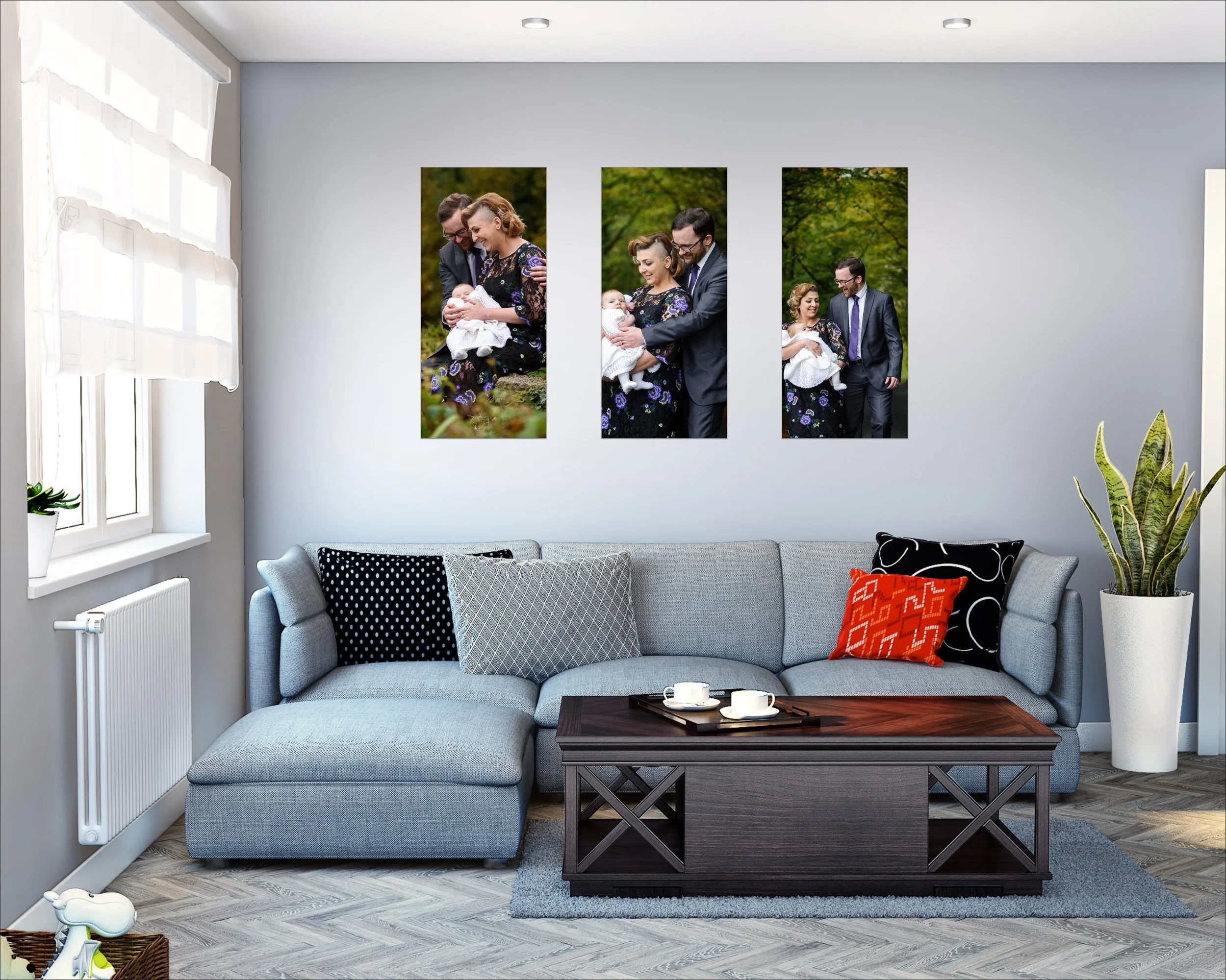 Living room with gray sectional sofa, decorative pillows, wooden coffee table with two cups, houseplant, and three framed family photos of a couple with a baby on the wall.