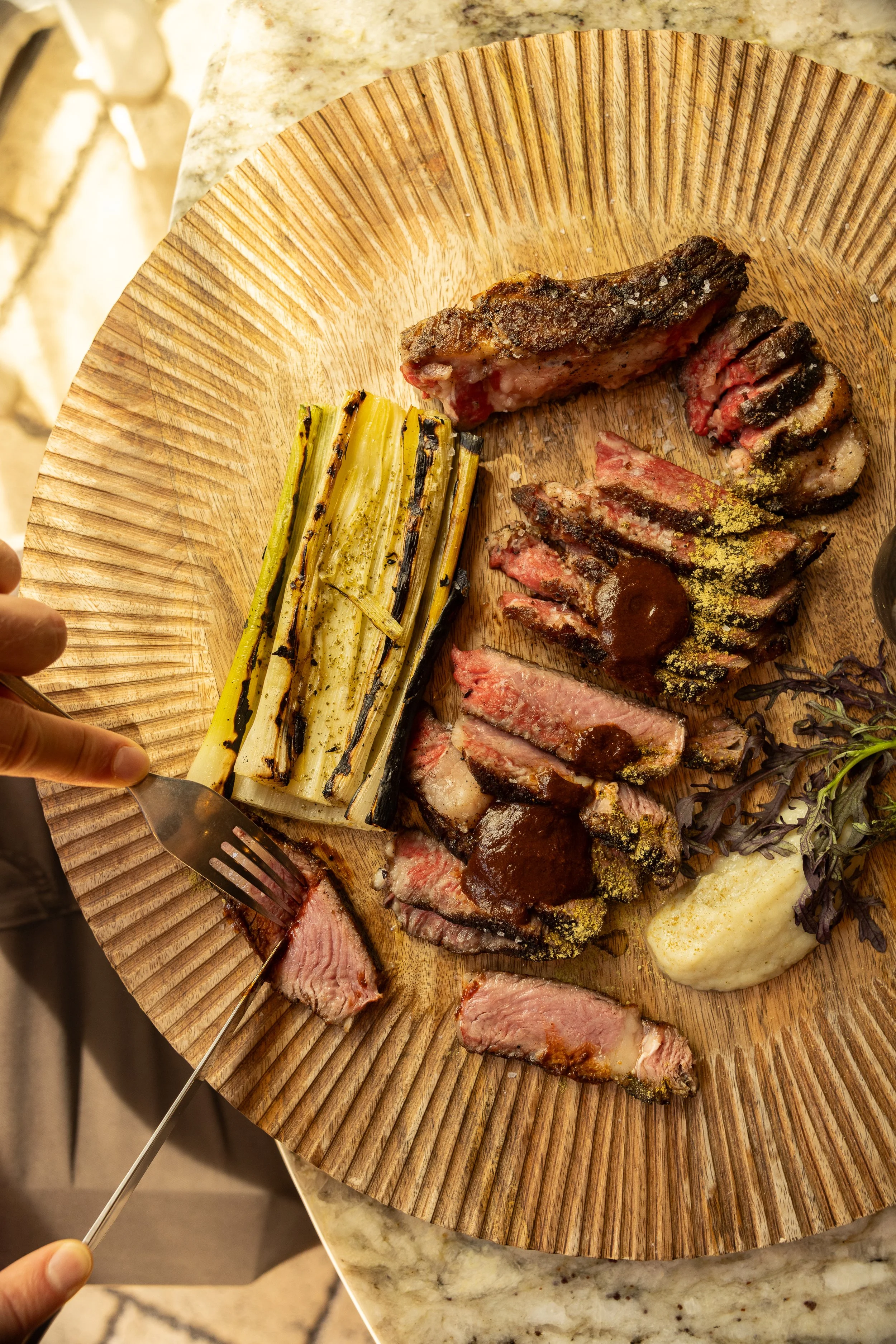 Sliced medium-rare steak with grill marks, charred asparagus, and a dollop of white sauce on a wooden serving board.